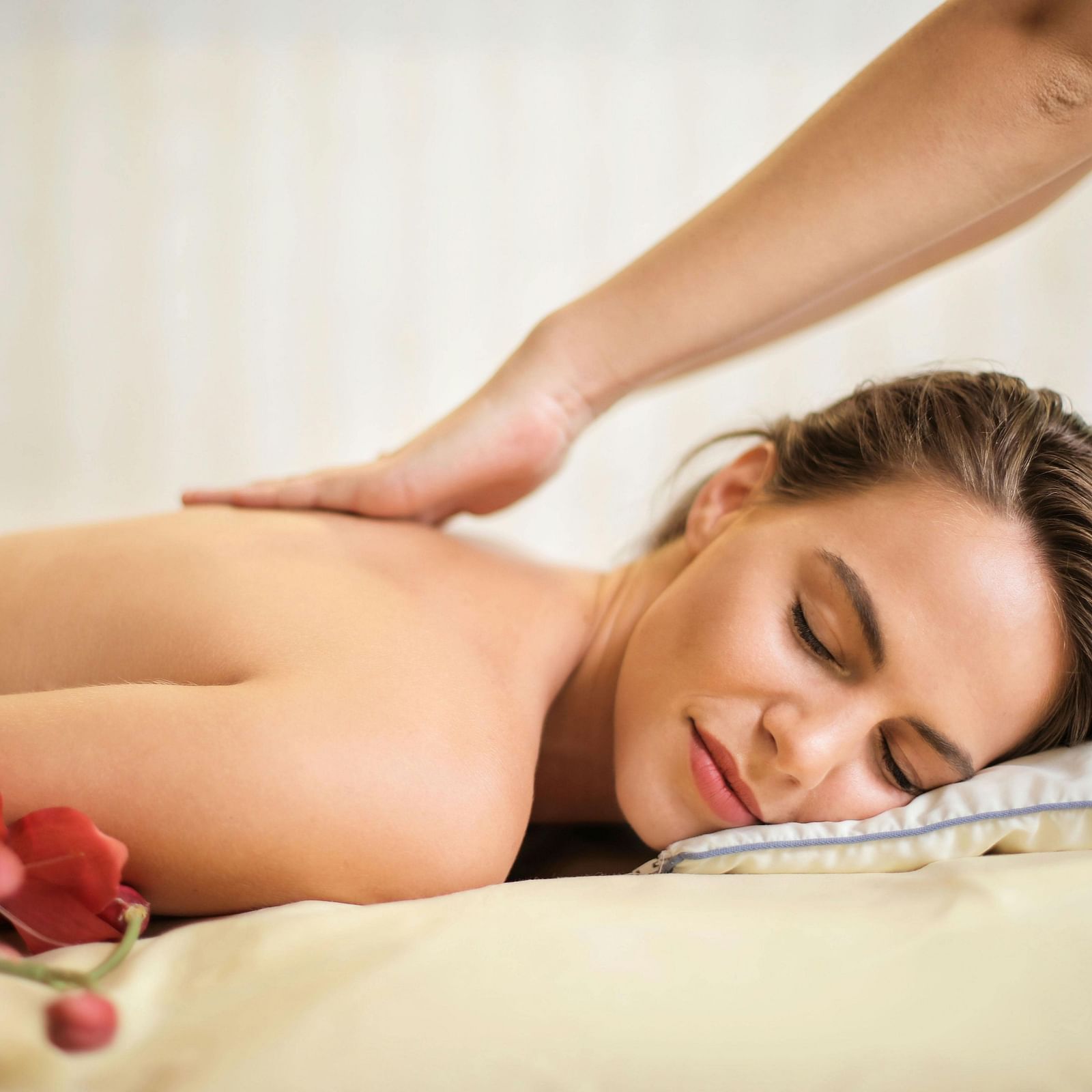An woman lying on her stomach on a massage table getting a back massage with flowers placed beside her.