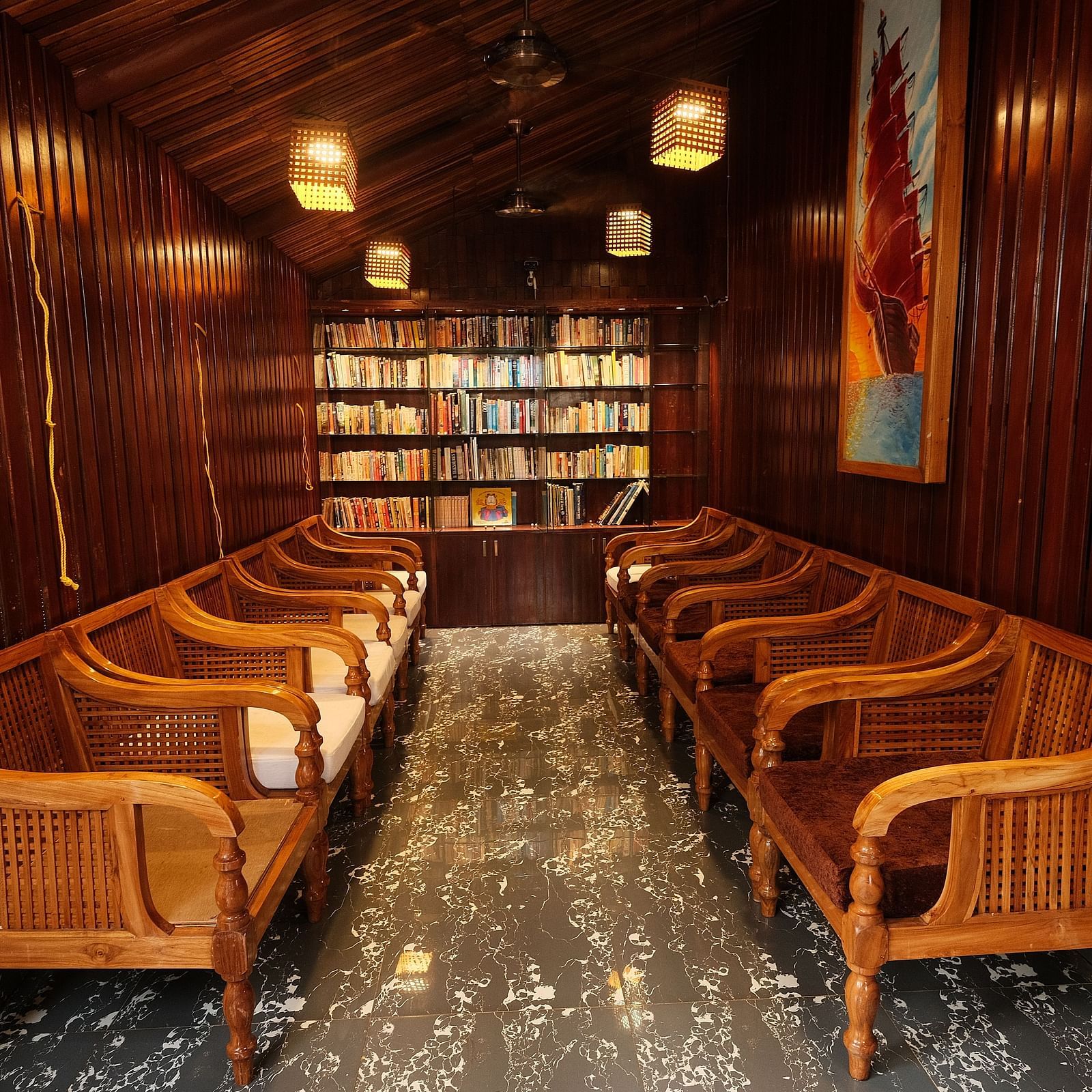 A cosy seating area inside a restaurant, with wooden benches and bookshelves lining the walls | Fusion Cafe and Multi-cuisine | RainForest Resort, Port Blair, Andaman and Nicobar Island