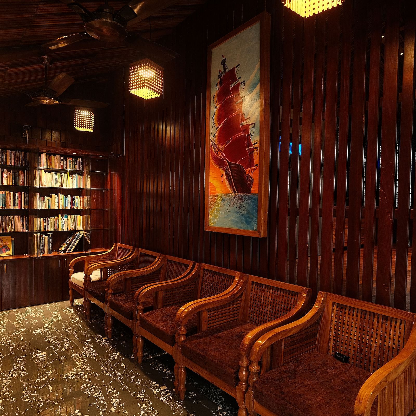 An interior of a restaurant with wooden chairs placed near bookshelves | Fusion Cafe and Multi-cuisine | RainForest Resort, Port Blair, Andaman and Nicobar Island