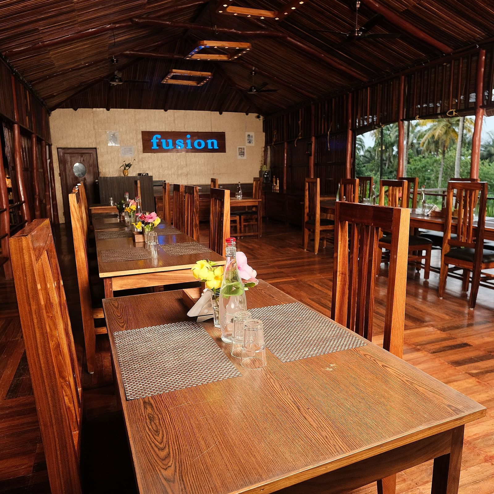 A wooden interior is viewed from a high angle, showcasing tables, chairs, and an open doorway to the outside | Fusion Cafe and Multi-cuisine | RainForest Resort, Port Blair, Andaman and Nicobar Island