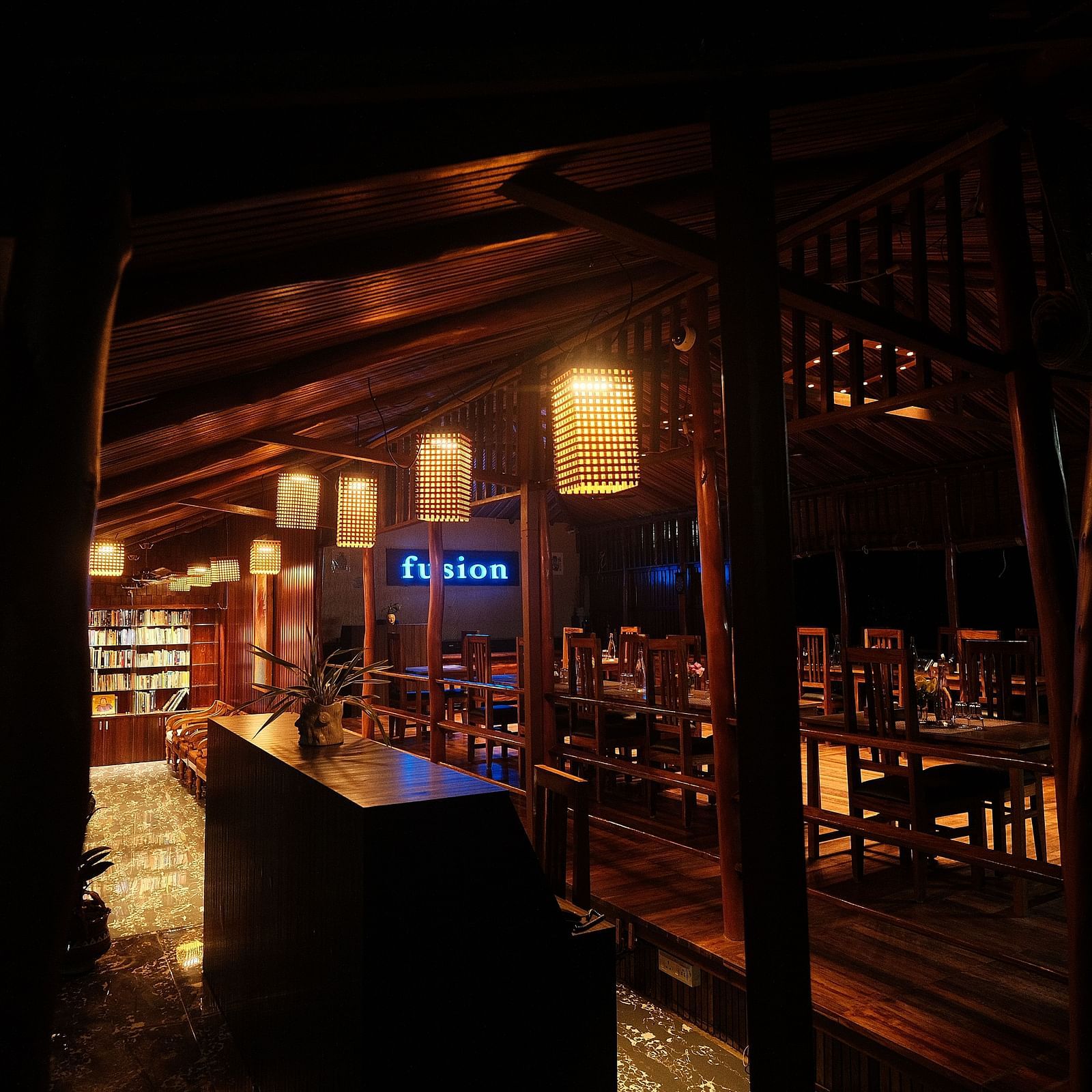 A dimly lit wooden interior features seating and shelving, with hanging lamps providing a warm ambience | Fusion Cafe and Multi-cuisine | RainForest Resort, Port Blair, Andaman and Nicobar Island