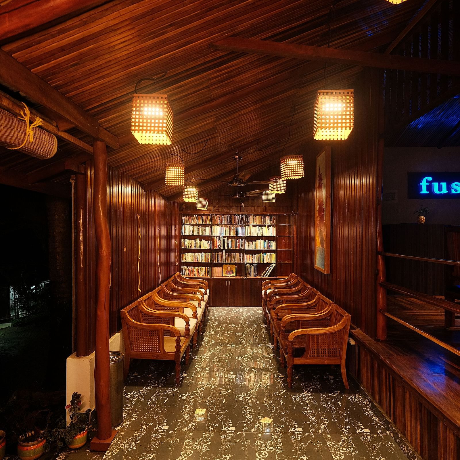 A dimly lit wooden interior features rows of seating and shelves, illuminated by hanging lamps | Fusion Cafe and Multi-cuisine | RainForest Resort, Port Blair, Andaman and Nicobar Island