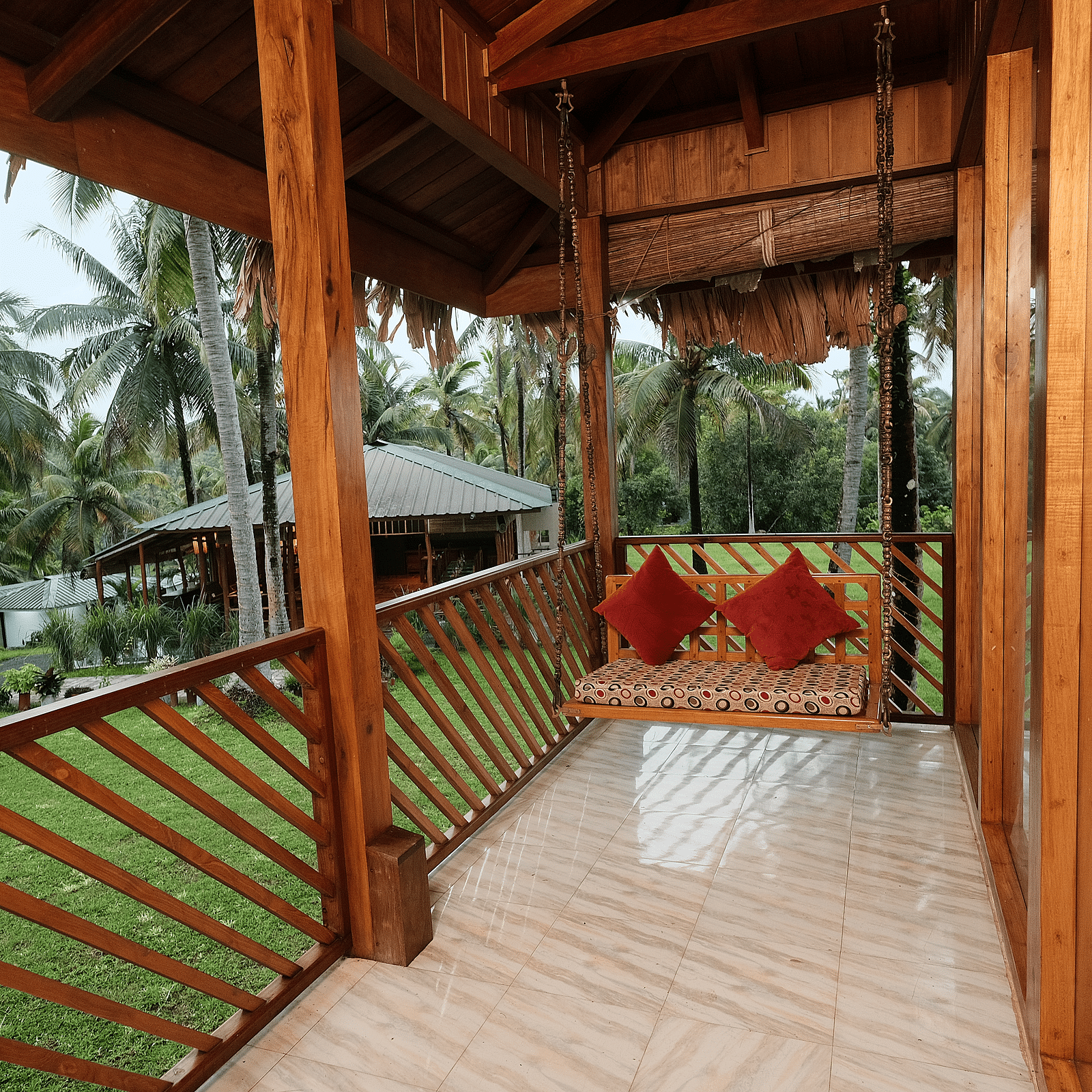 A close-up of a rustic wooden gazebo or porch with a thatched roof, featuring red cushions on a swing seat.