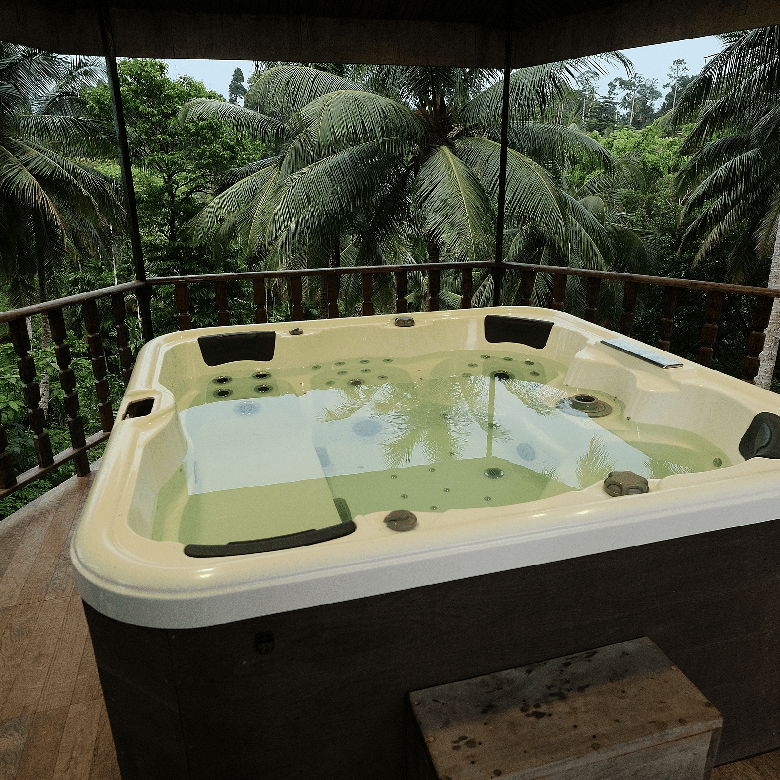 An outdoor jacuzzi on a wooden deck, surrounded by lush green palm trees and tropical foliage.