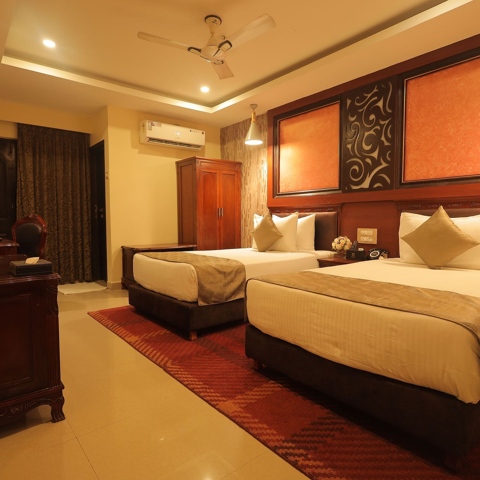 An image of a twin beds with bedside table, a set of table and chairs, flat TV screen, and AC - Sathyam Grand Resort