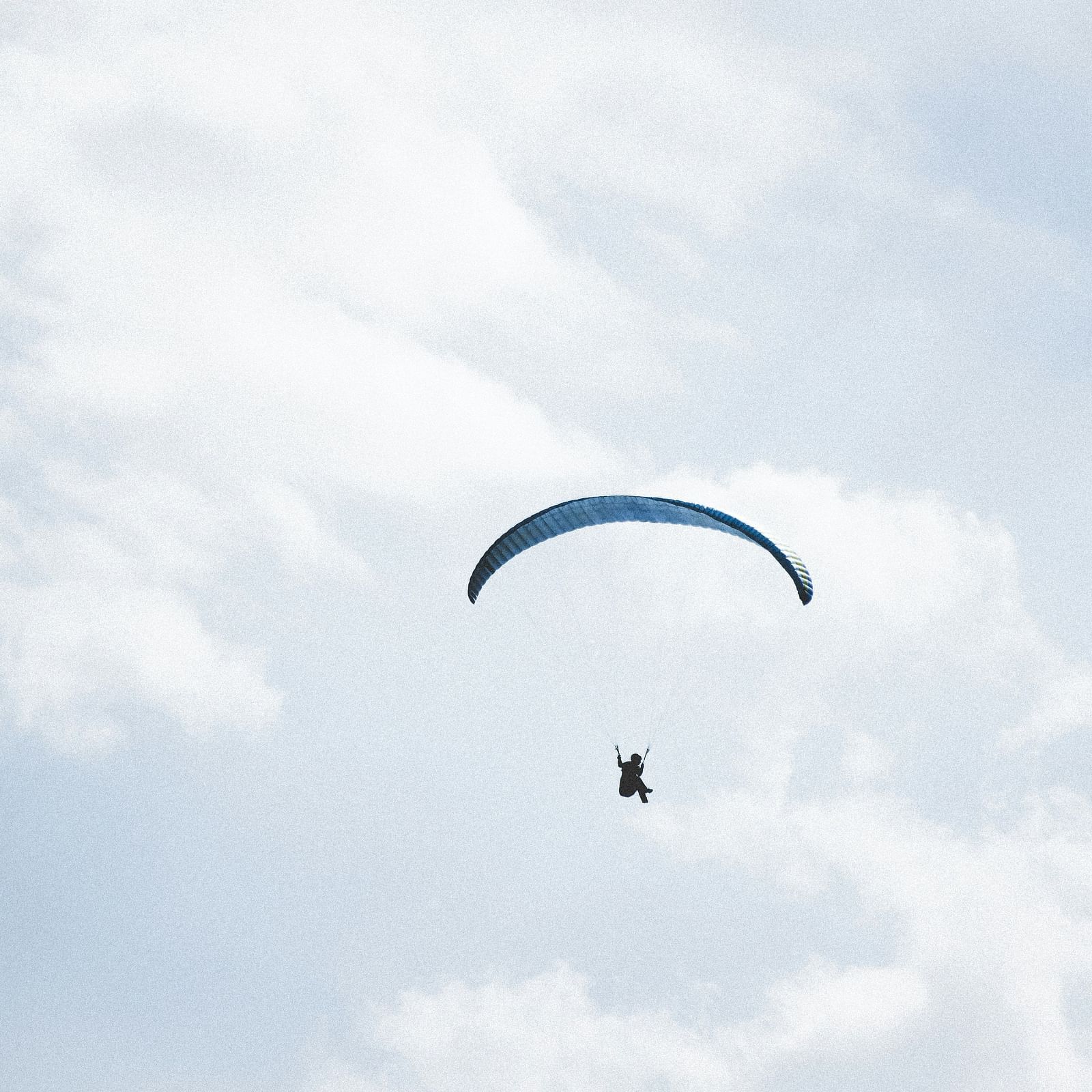 A view from below of a person paragliding with blue sky in the background