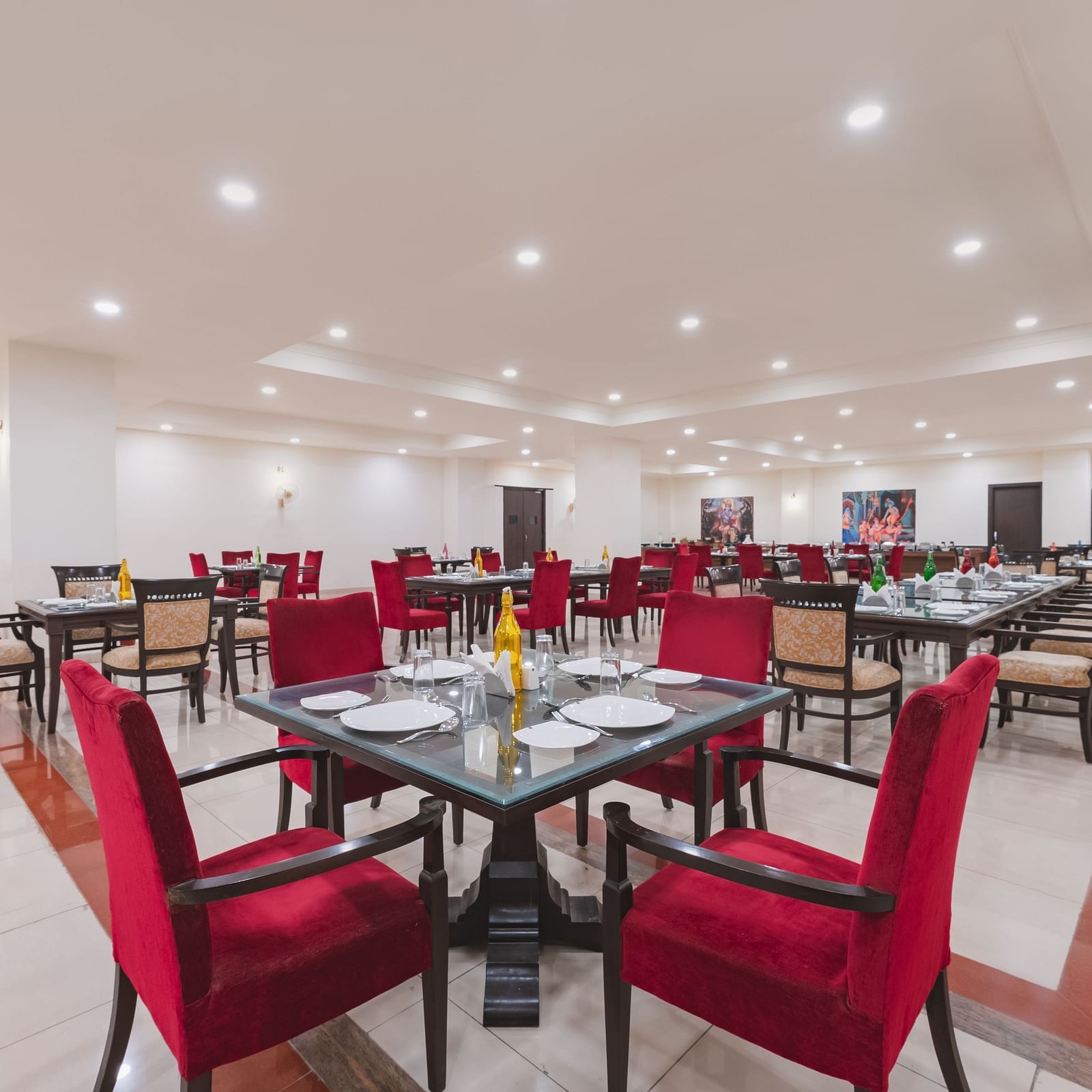 A closer view of a dining table featuring red chairs and tableware in a well lit dining space at Shri Vallabh Vilas Lords Plaza Nathdwara.