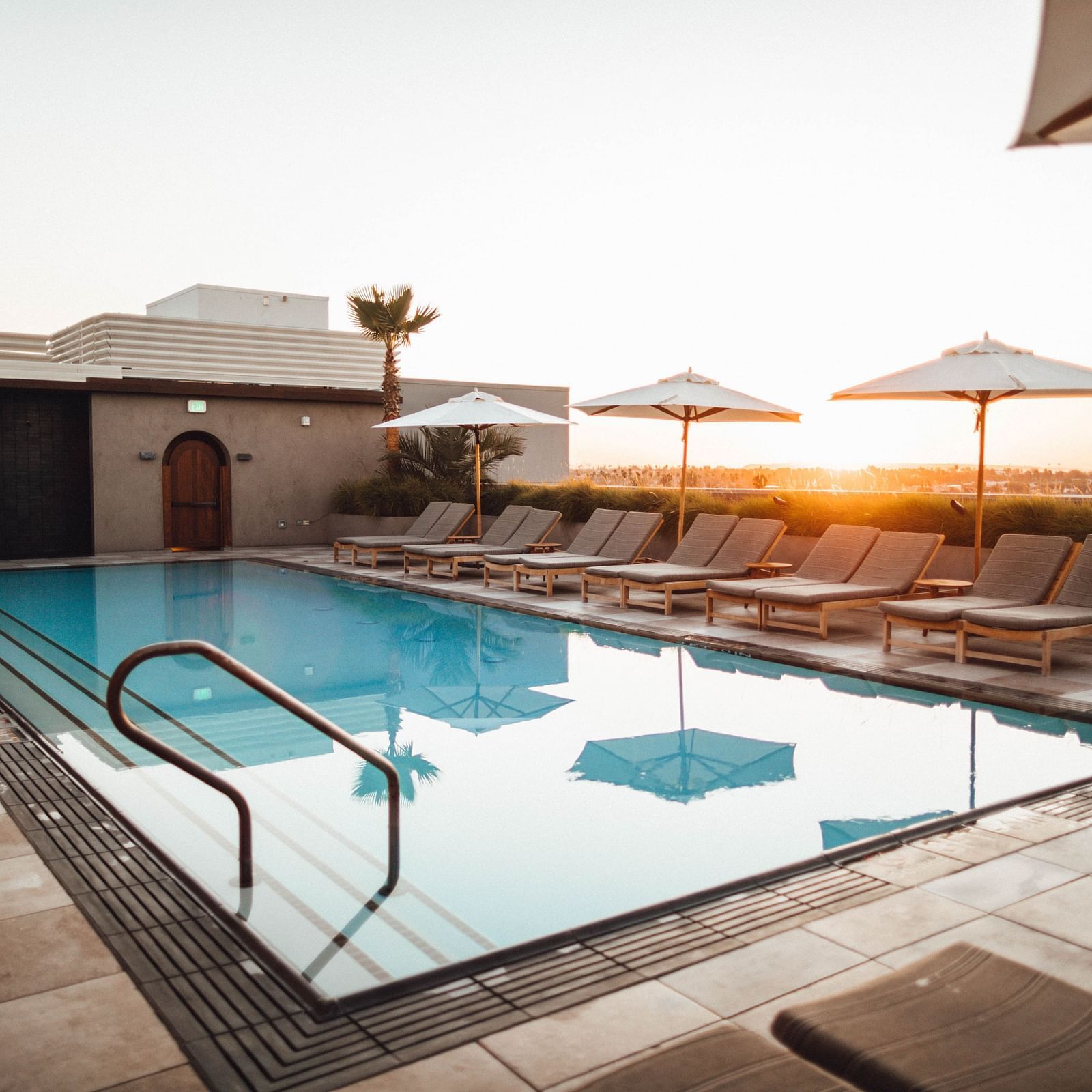 A swimming pool with loungers next to it and the sun setting in the background