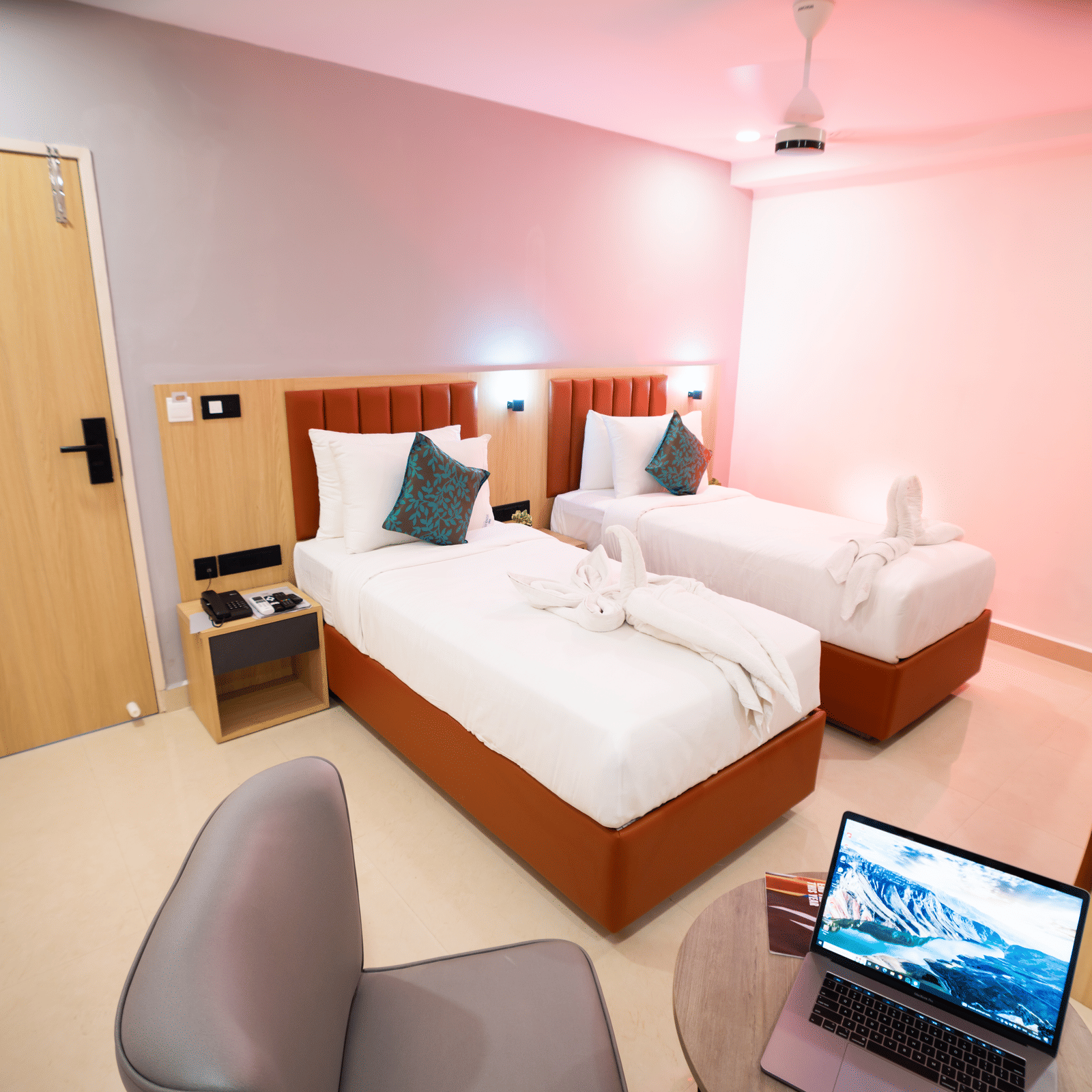 View of a room with twin beds and a laptop on a small round table with chairs on either side at Sunrise Business Hotel, Hyderabad.