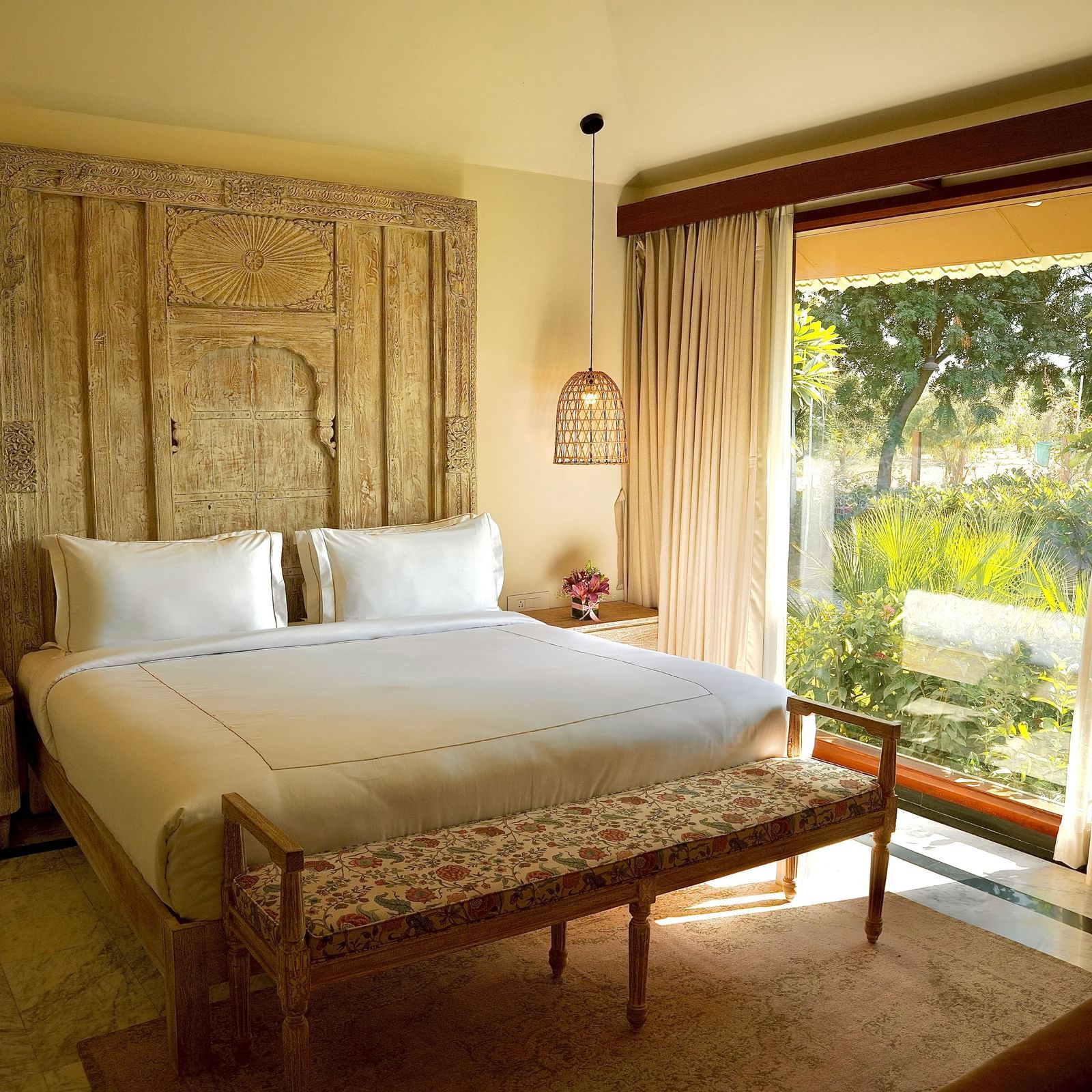 Well lit bedroom with a comfortable king bed, wall decor and curtained windows overlooking greenery at Surpura Bagh.