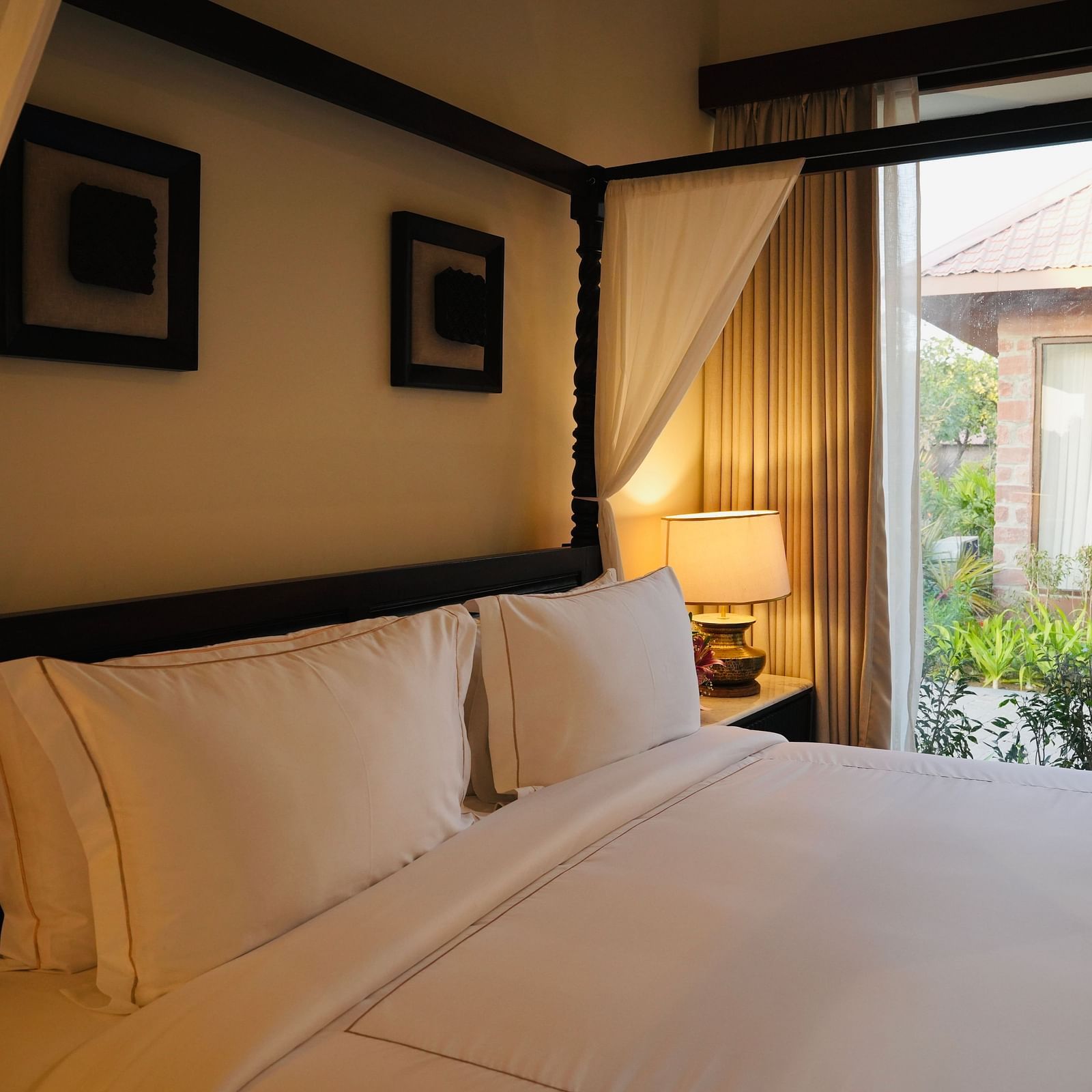 A bedroom with neatly arranged bed and photo frames on the wall and a view outside through the window.