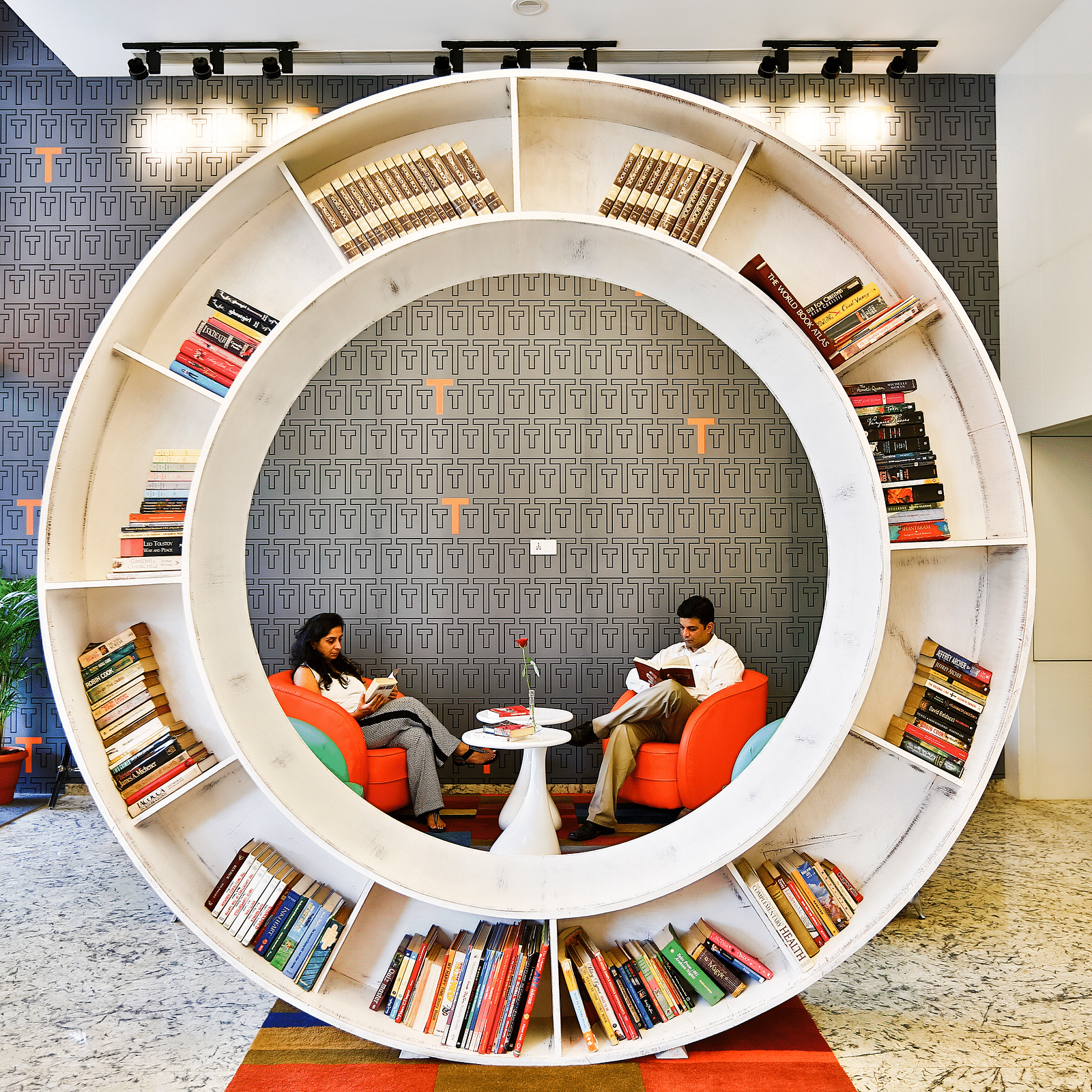 Two people sitting on sofa chairs reading books in a library with a circular book shelf placed in the middle at T24 Residency, Andheri East, Mumbai