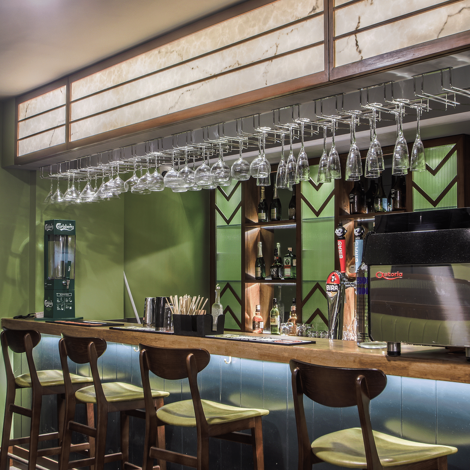 Shot of a bar with a wooden countertop, green walls, and a row of stools  | T24 Retro