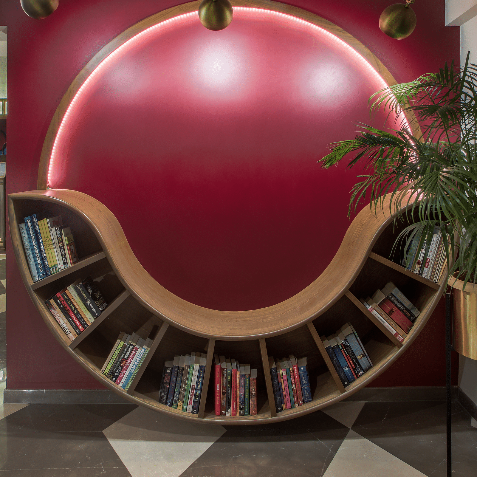 A unique, curved wooden bookshelf with a red wall behind it. The bookshelf is shaped like a wave and is filled with books.