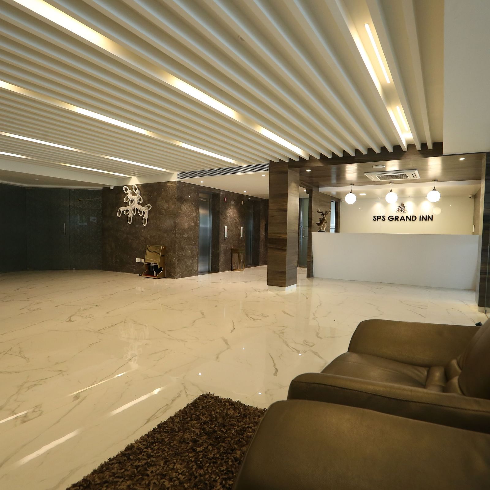 A spacious, well-lit lobby area with modern ceiling lights, light-coloured flooring, and comfortable lounge seating - TGI SPS Grand, Coimbatore