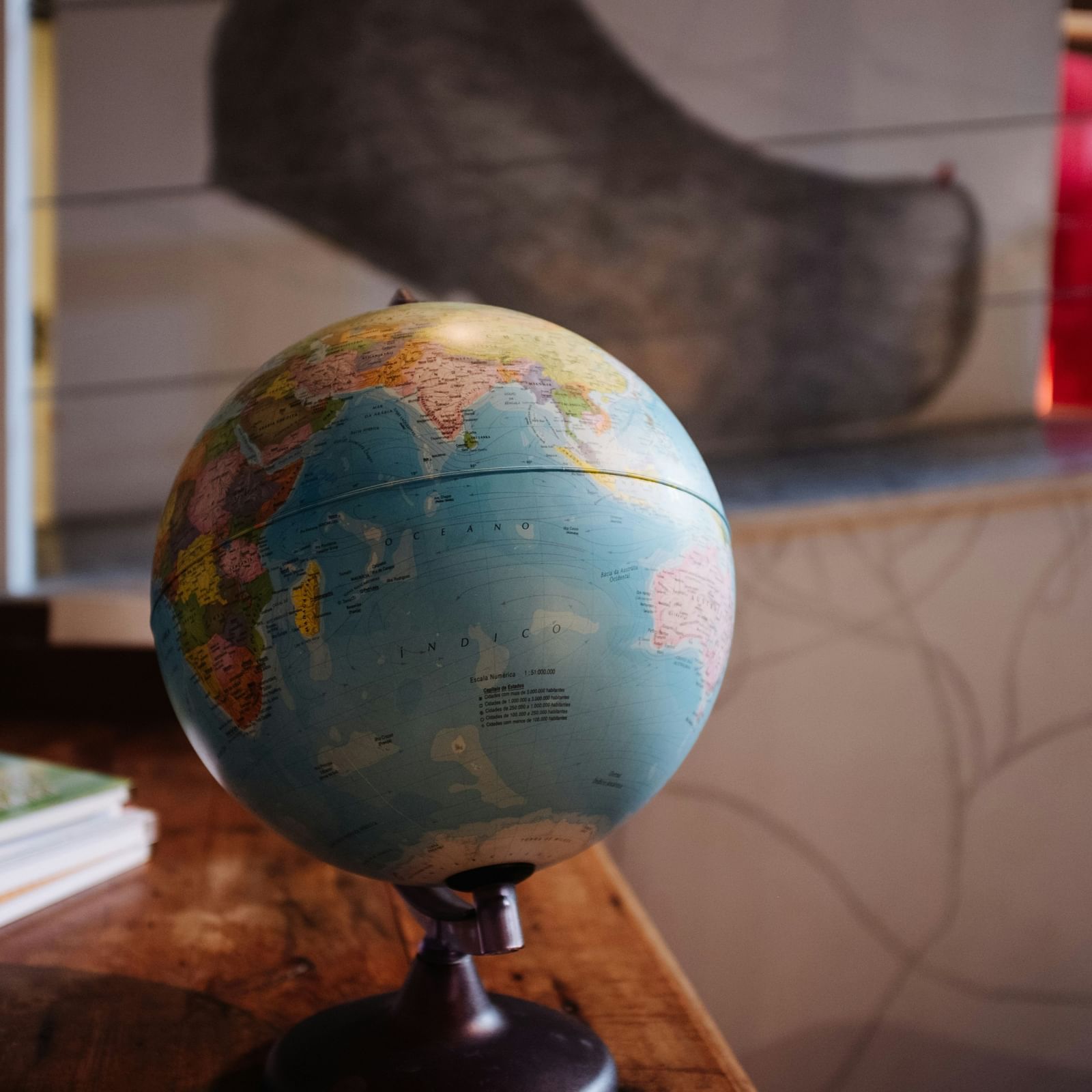 A globe kept on a table with books behind it.