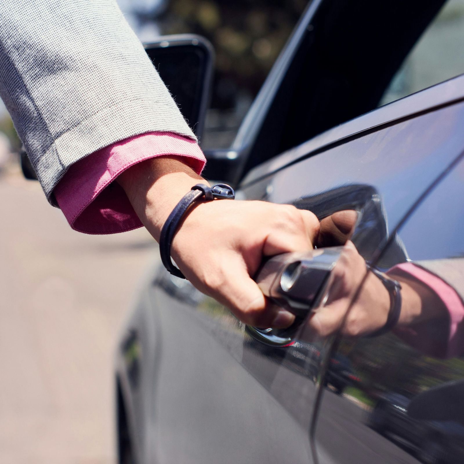 A person dressed in business formals opening the door of a car.