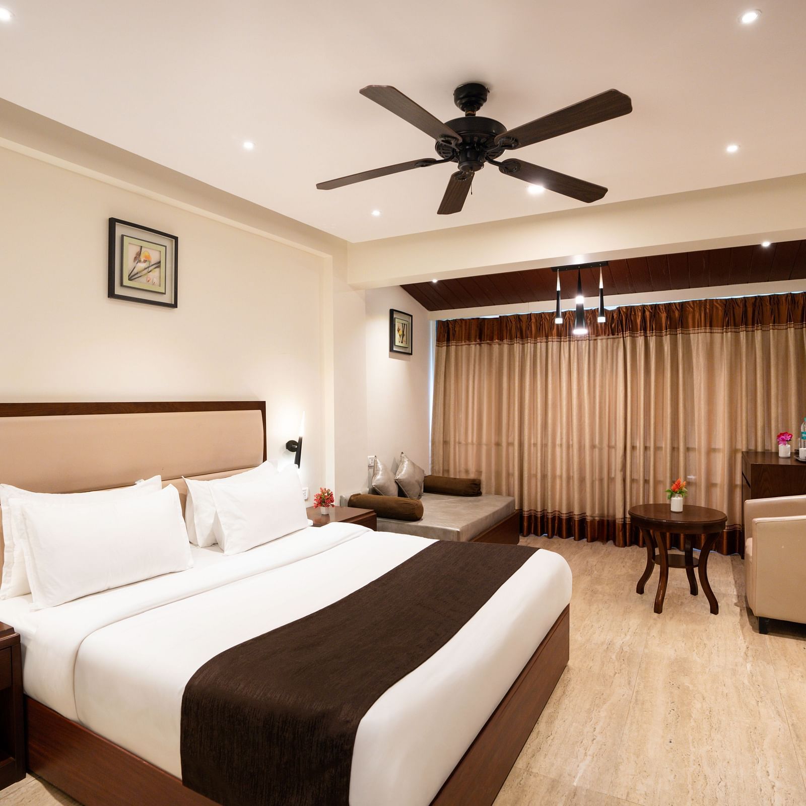 Spacious room with double bed, ceiling fan, and a sitting area with table - The Grand Legacy Resort & Spa