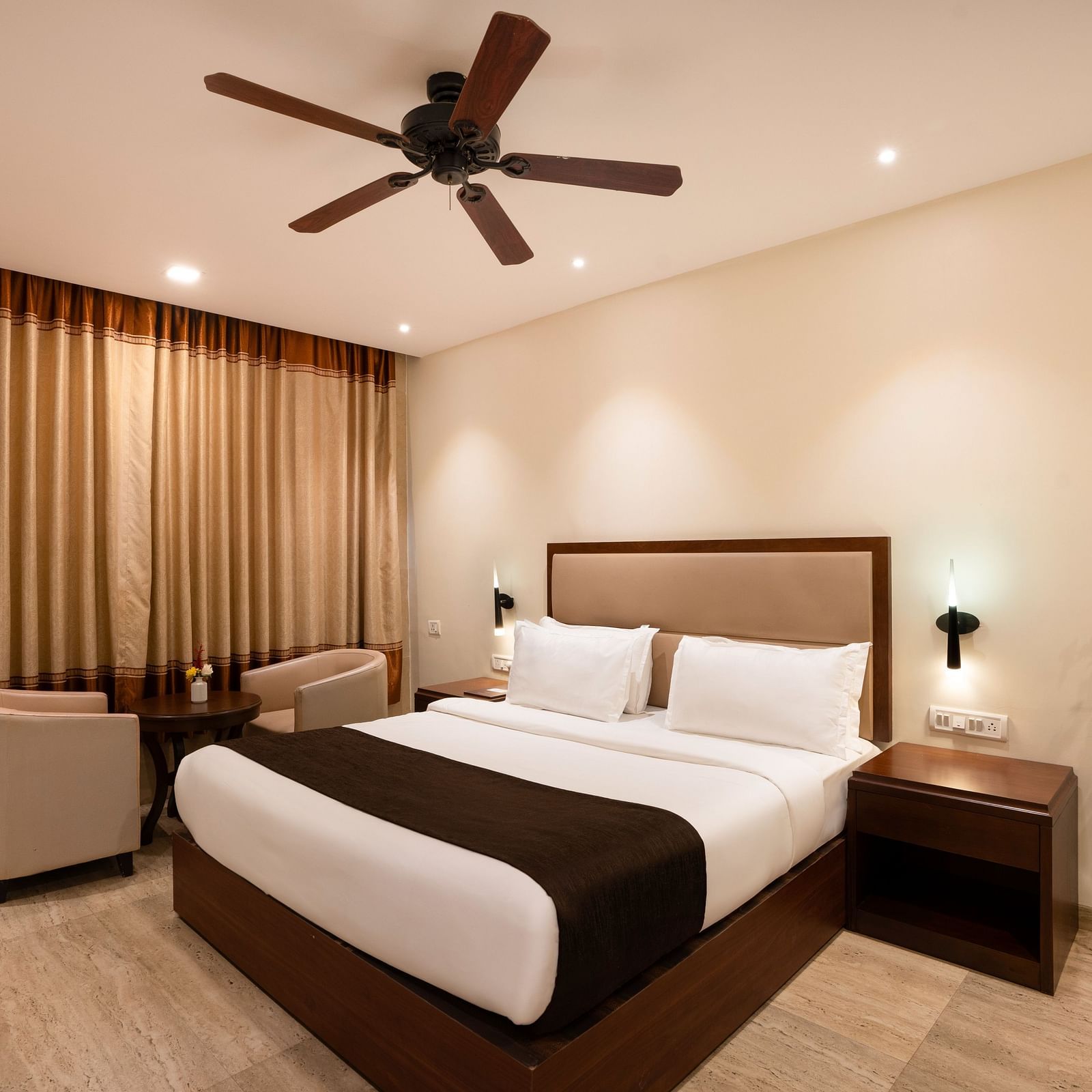 Shot of a spacious room with neutral toned walls featuring a king size bed, two small sofas, a centre table, flower vase and a side table | The Grand Legacy Resort and Spa