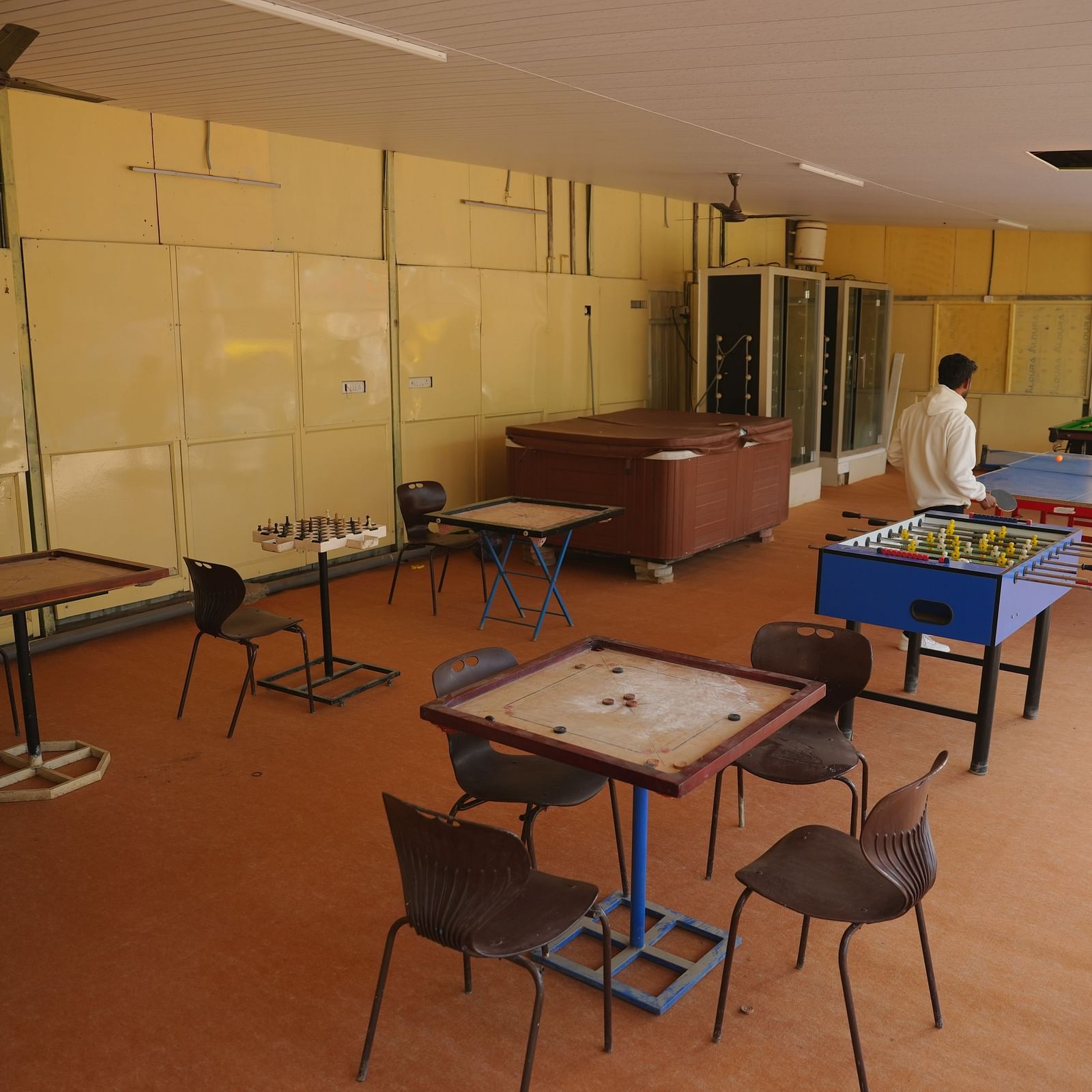 A game room with carrom boards placed on a table surrounded with chairs at The Meenakshi Resort by Welcome Inn Hospitality, Bangalore.
