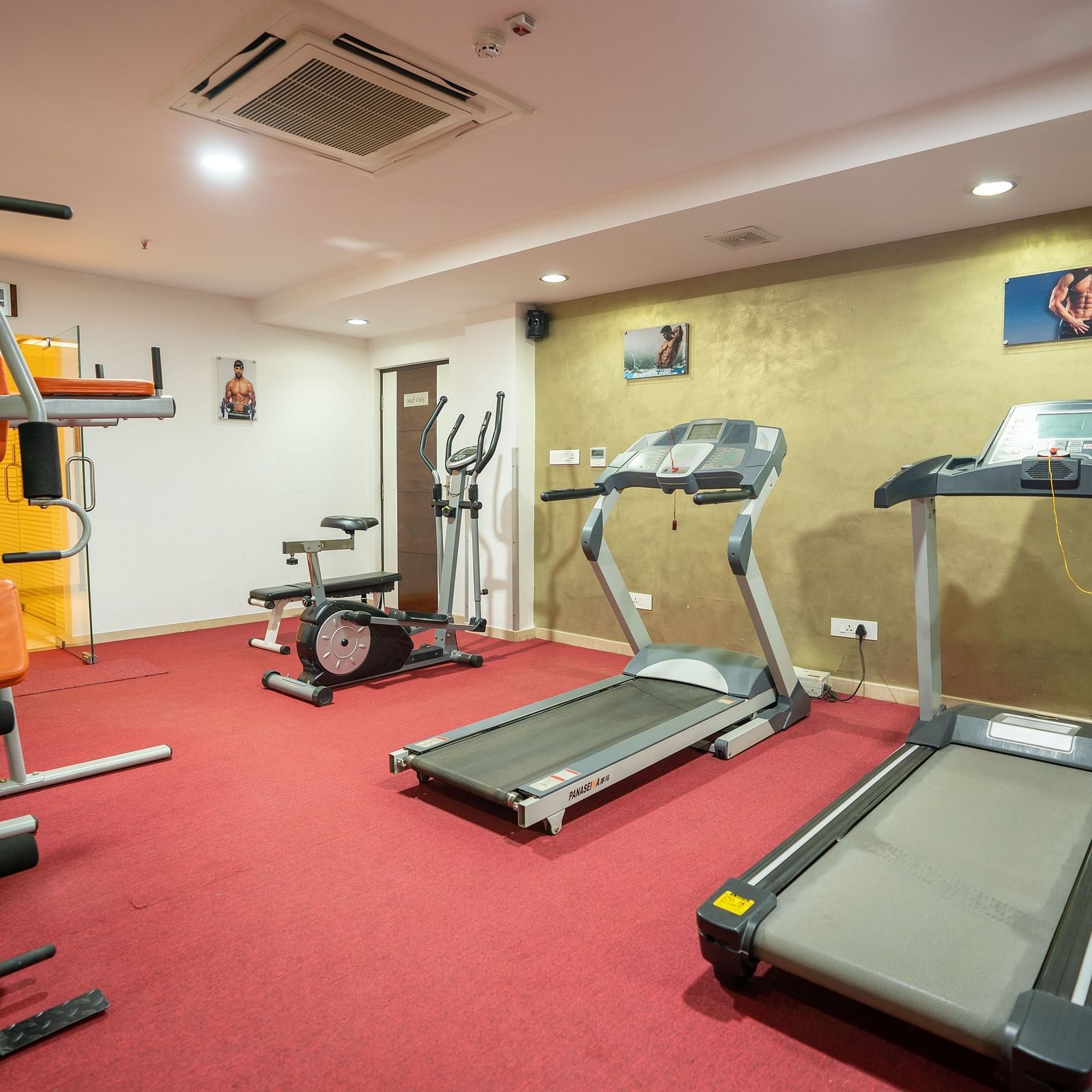 A well-equipped home gym with treadmills, a weight machine, and free weights at The President Hotel, Hubli