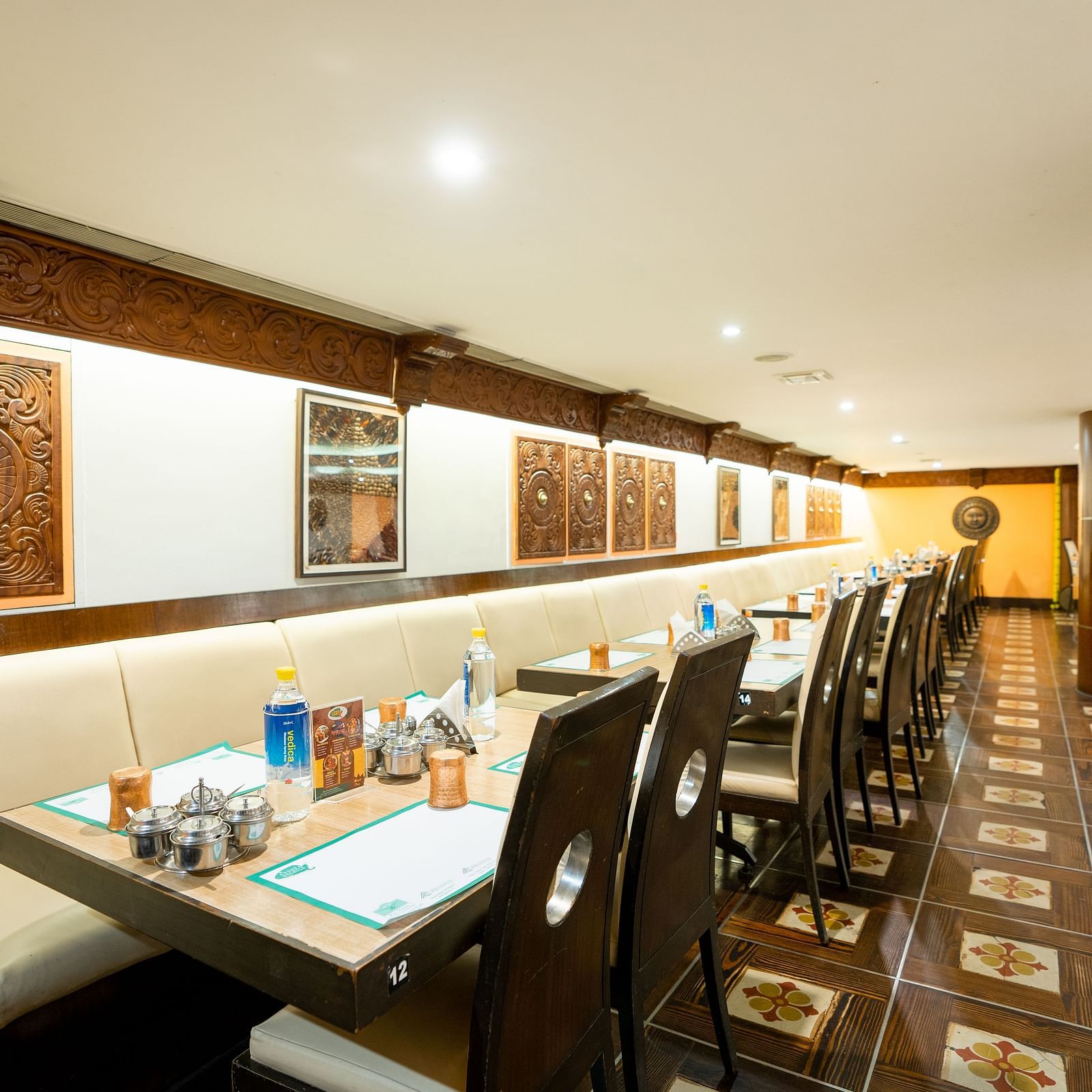 A spacious and well-lit restaurant interior with neatly arranged tables and chairs set for dining under a warm ambient lighting - The President Hotel Jayanagar, Bangalore