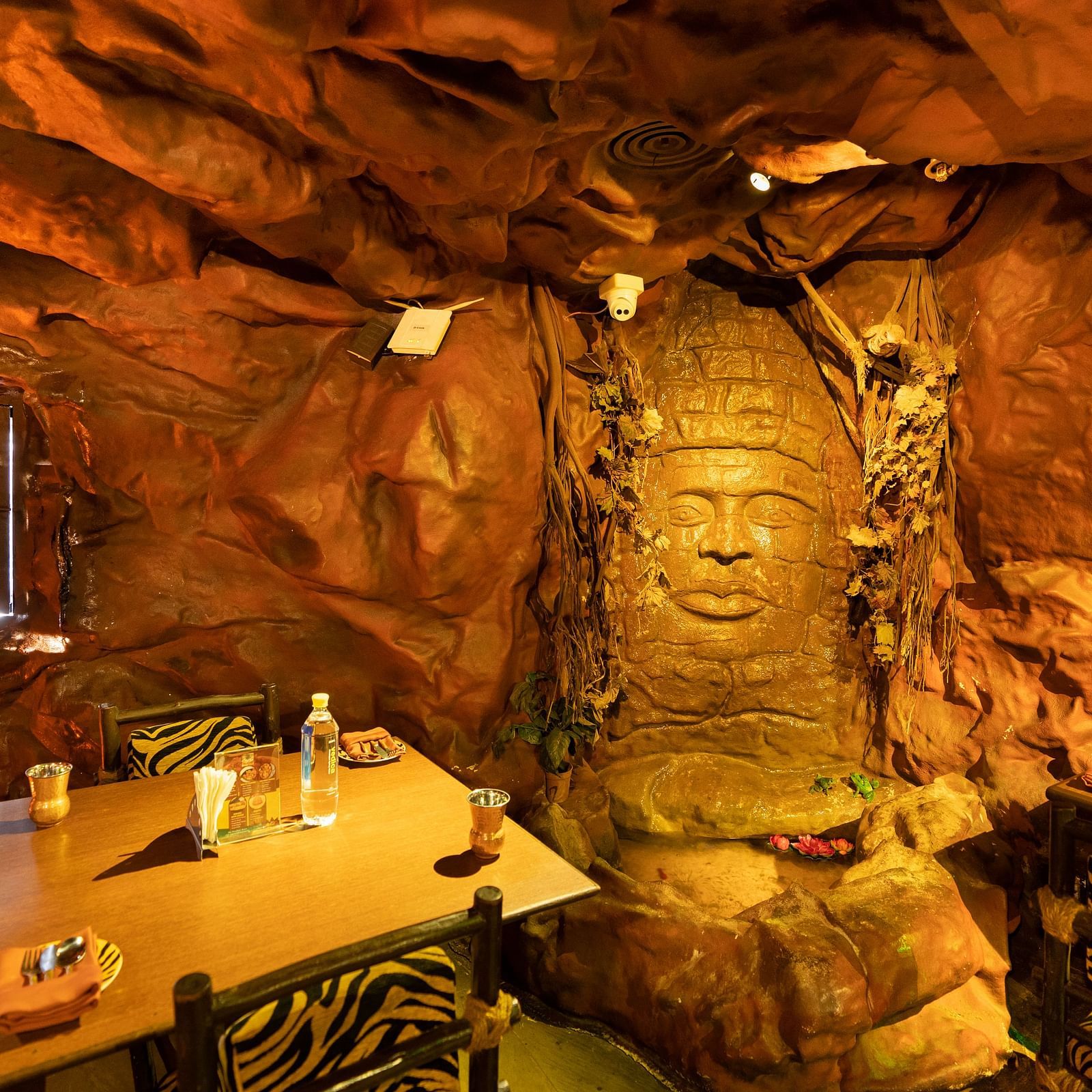 A unique restaurant with a cavernous atmosphere featuring a large Buddha face sculpture and textured walls, creating an immersive dining experience - The President Hotel Jayanagar, Bangalore