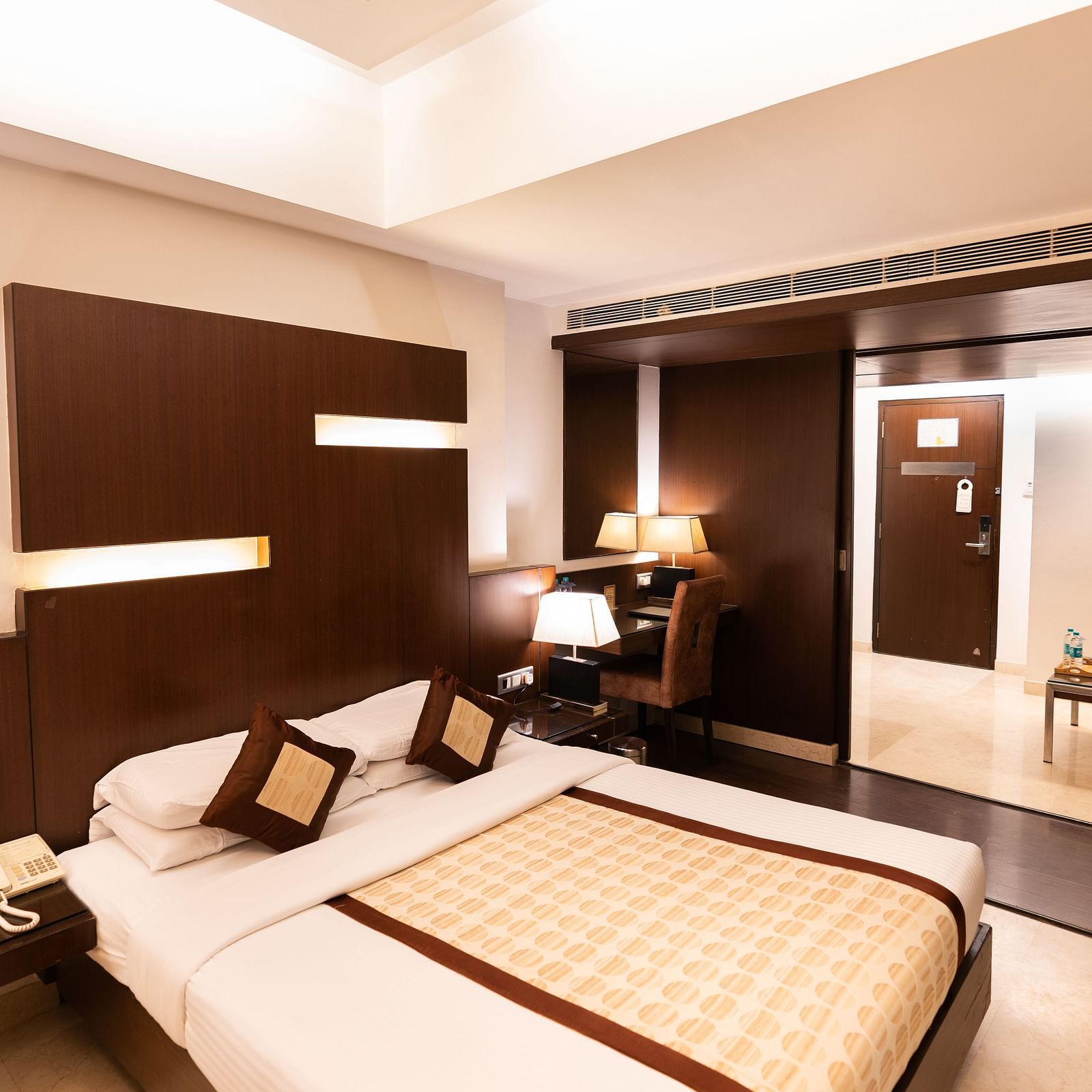 A modern hotel room featuring a large bed with brown headboard, sleek furnishings, and ambient lighting for a comfortable stay - The President Hotel Jayanagar, Bangalore