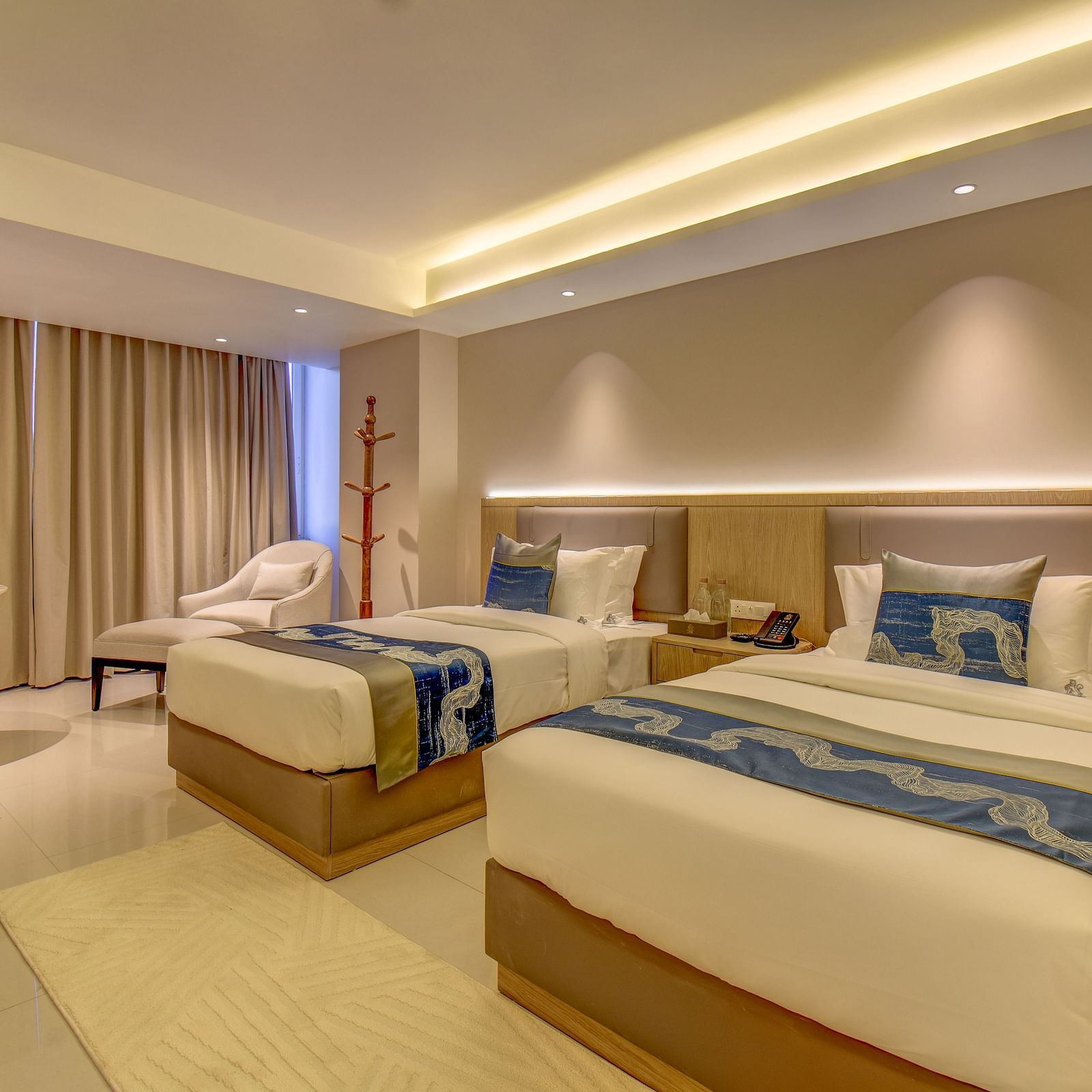 Side view of a well-lit Premium Twin room at The SSK Solitaire Boutique Hotel & Spa, Gangapur Road - Nashik featuring a twin  bed, two armchairs, a small table, and a work desk with a chair.