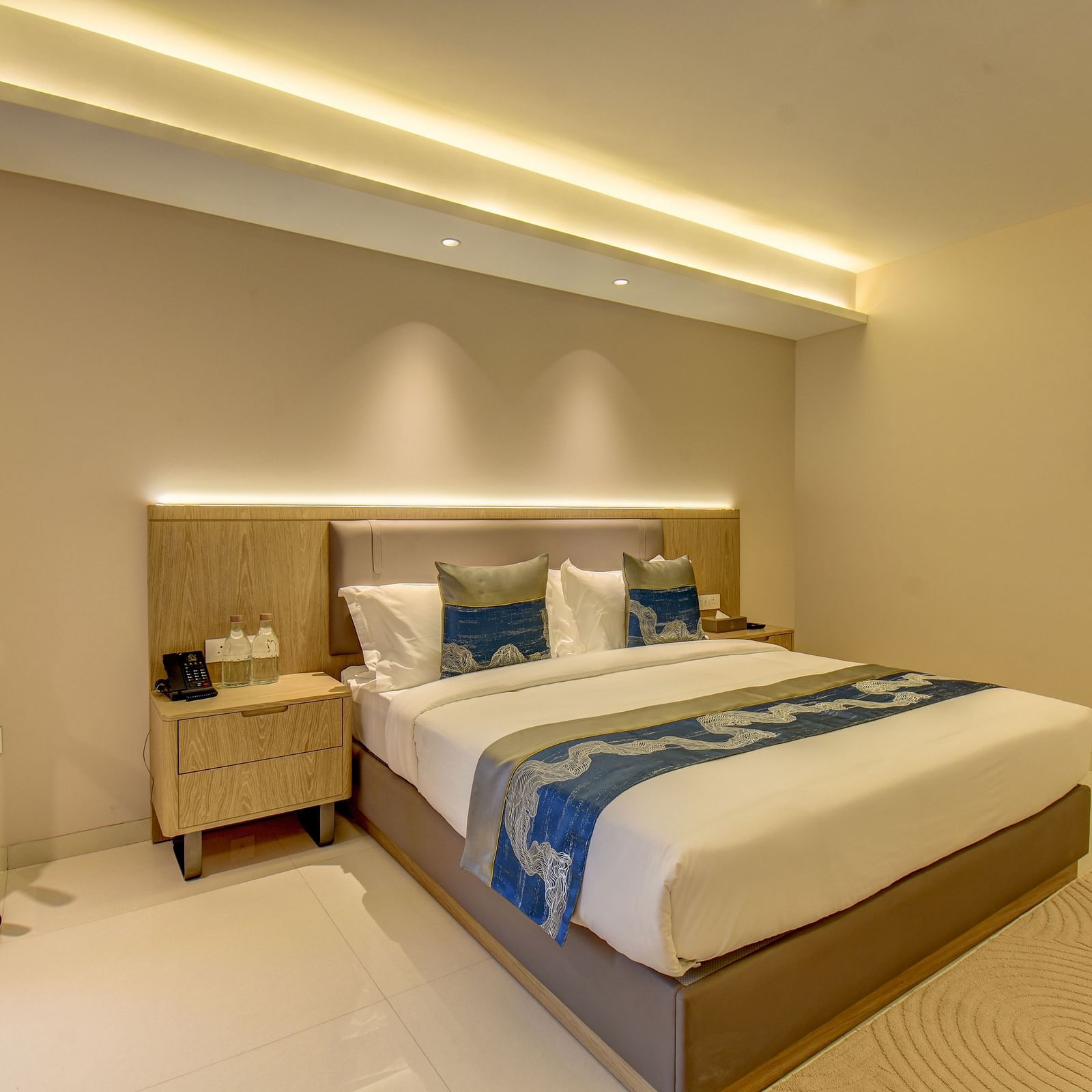 Side shot of a  well-lit Deluxe King room at The SSK Solitaire Boutique Hotel & Spa, Gangapur Road - Nashik featuring a king size  bed, two armchairs, a small table, and a work desk with a chair.