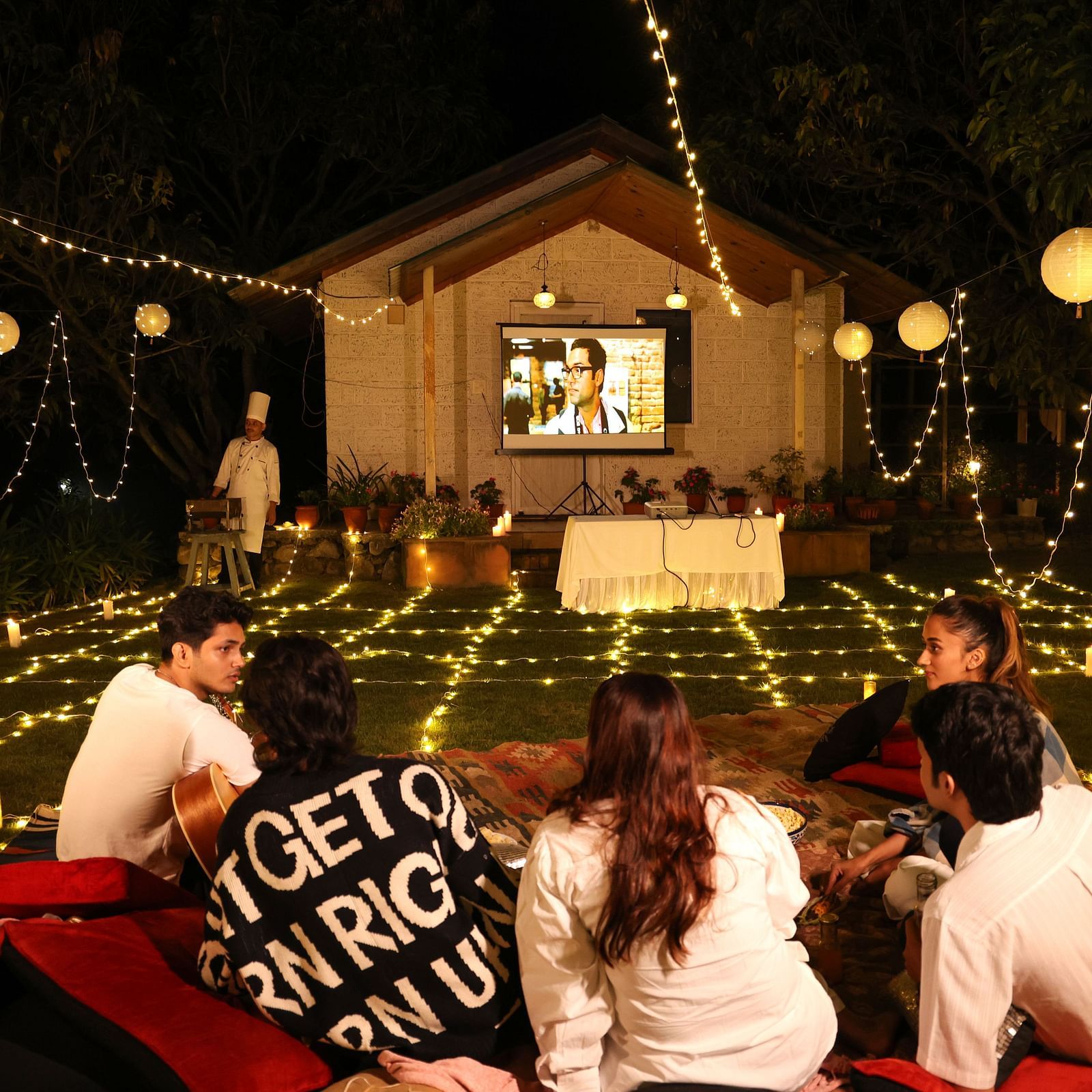 People enjoying an open movie night setup with lights and a projector set up at The Sylvan Retreat, Dehradun. 