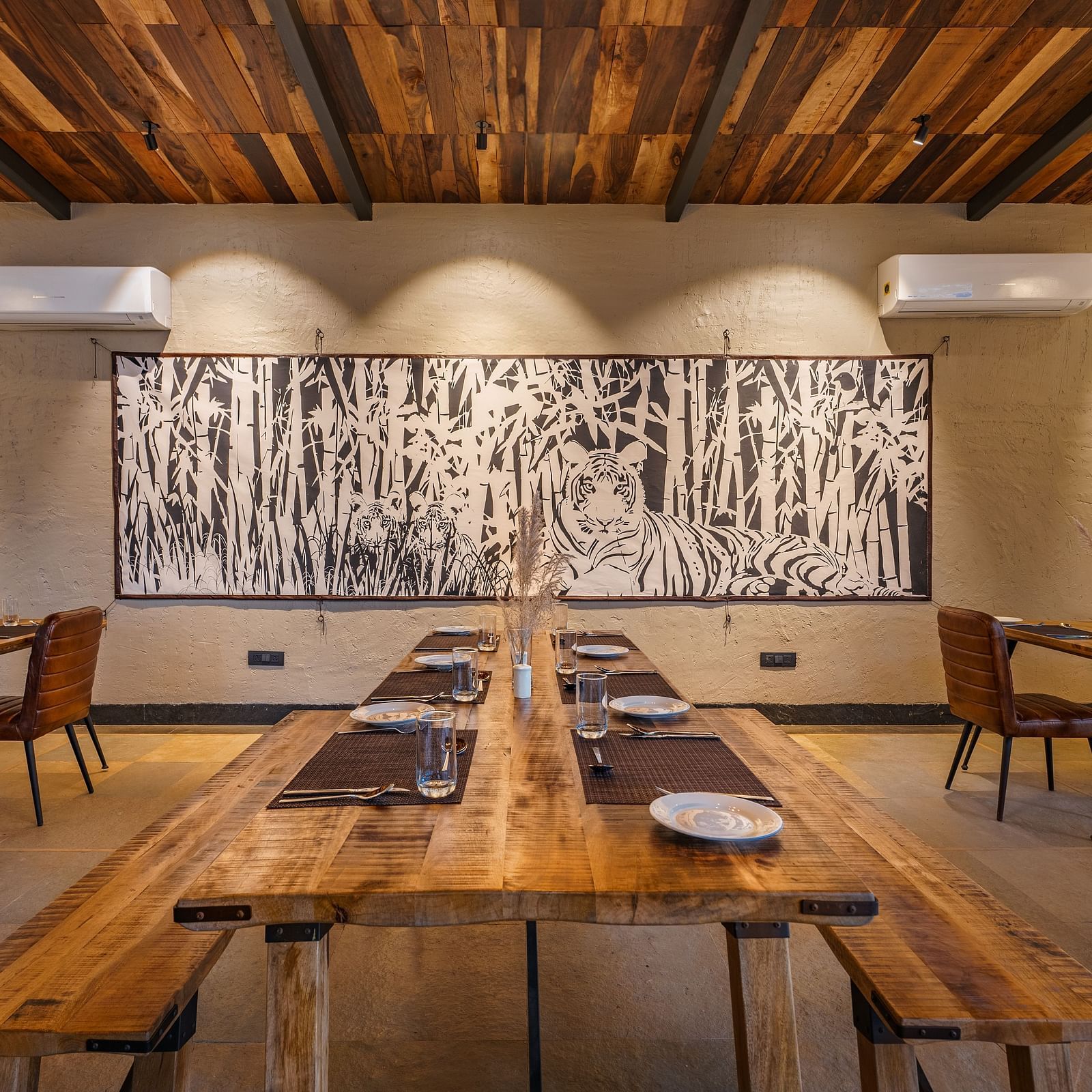 A wide view of a dining area with wooden table, benches and chairs at Trees N Tigers, Tadoba.