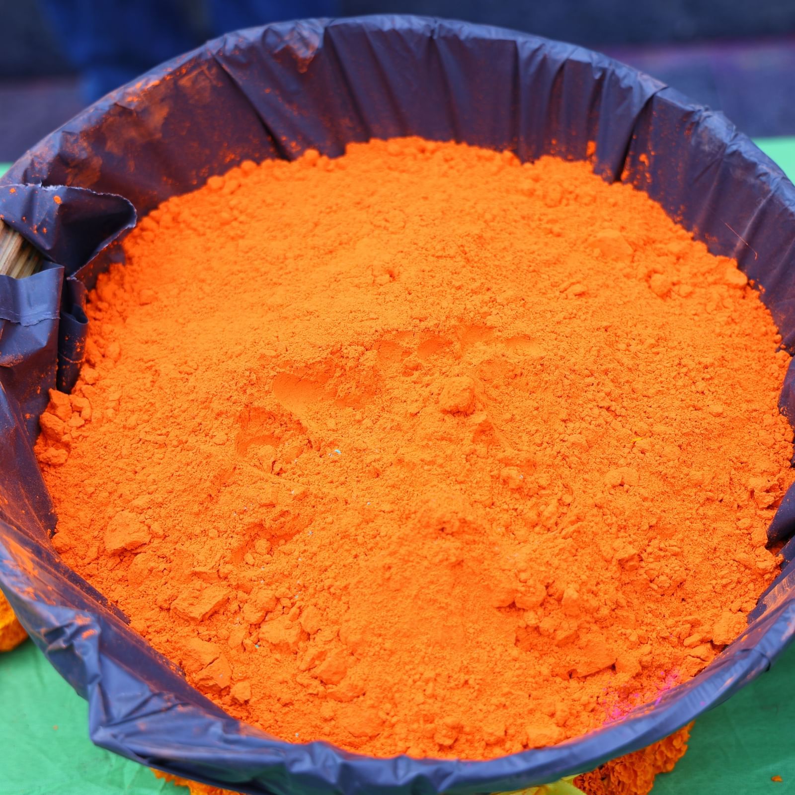 A large container filled with vibrant orange powder is placed on a green surface