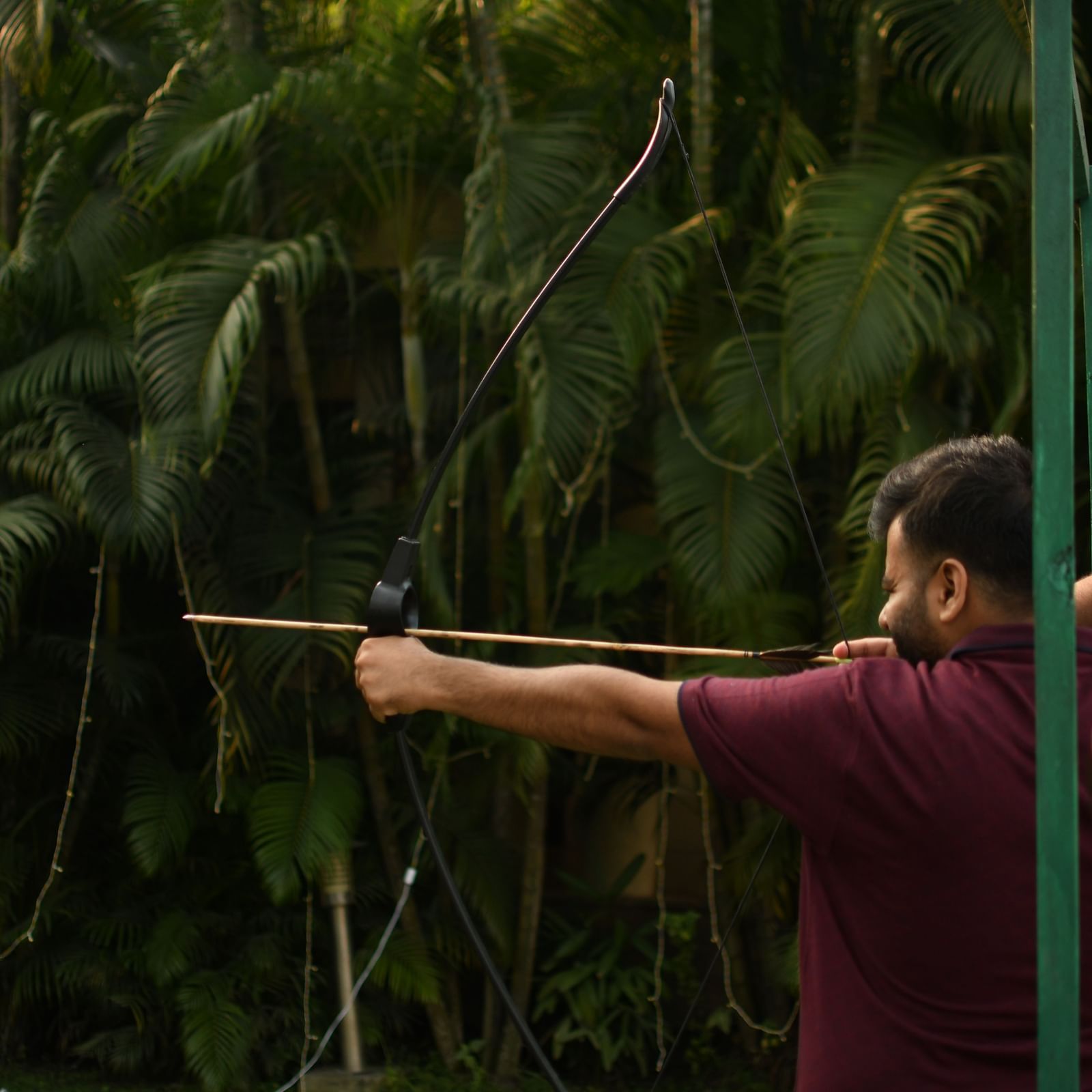 A person aims a long blowgun or similar weapon in a dense, green, natural environment