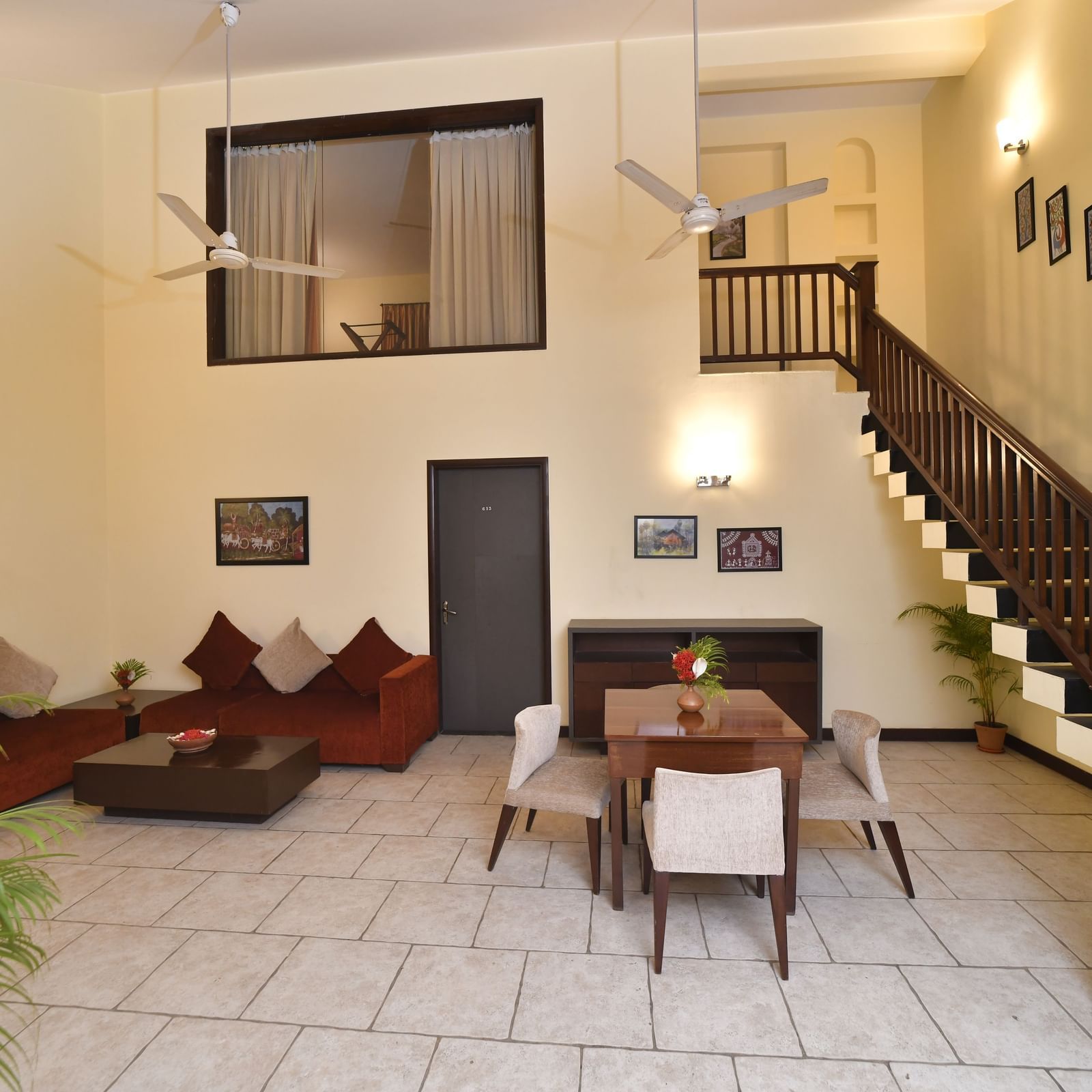 A living room with high ceilings includes a staircase, comfortable sofas, and a dining table set for a meal Green Villas