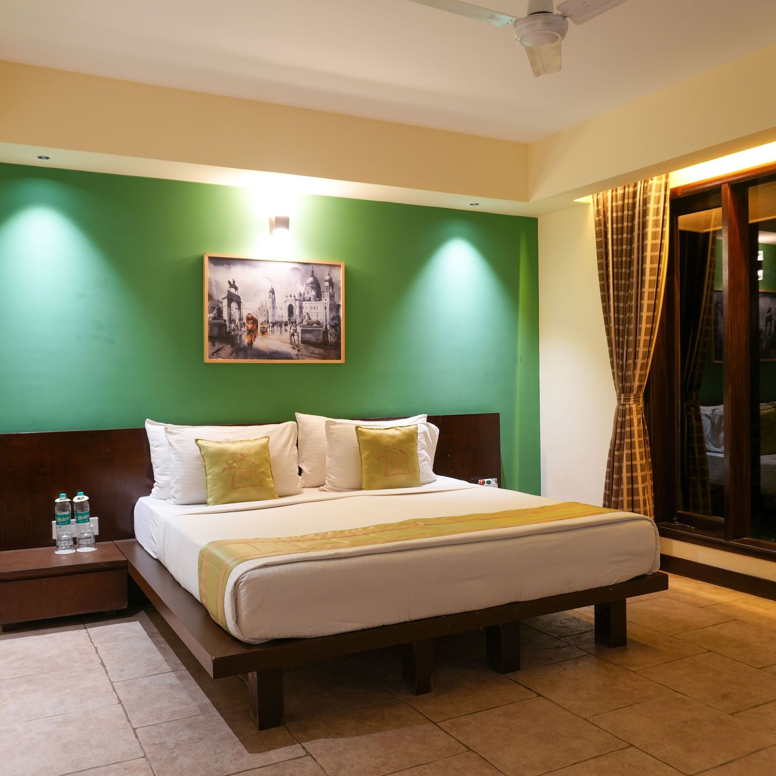 Bedroom in the Retreat Villa at Vedic Village Spa Resort with a double bed, wooden headrest, ceiling fan, and a large wall-to-wall window offering a night-time view of the outdoors.