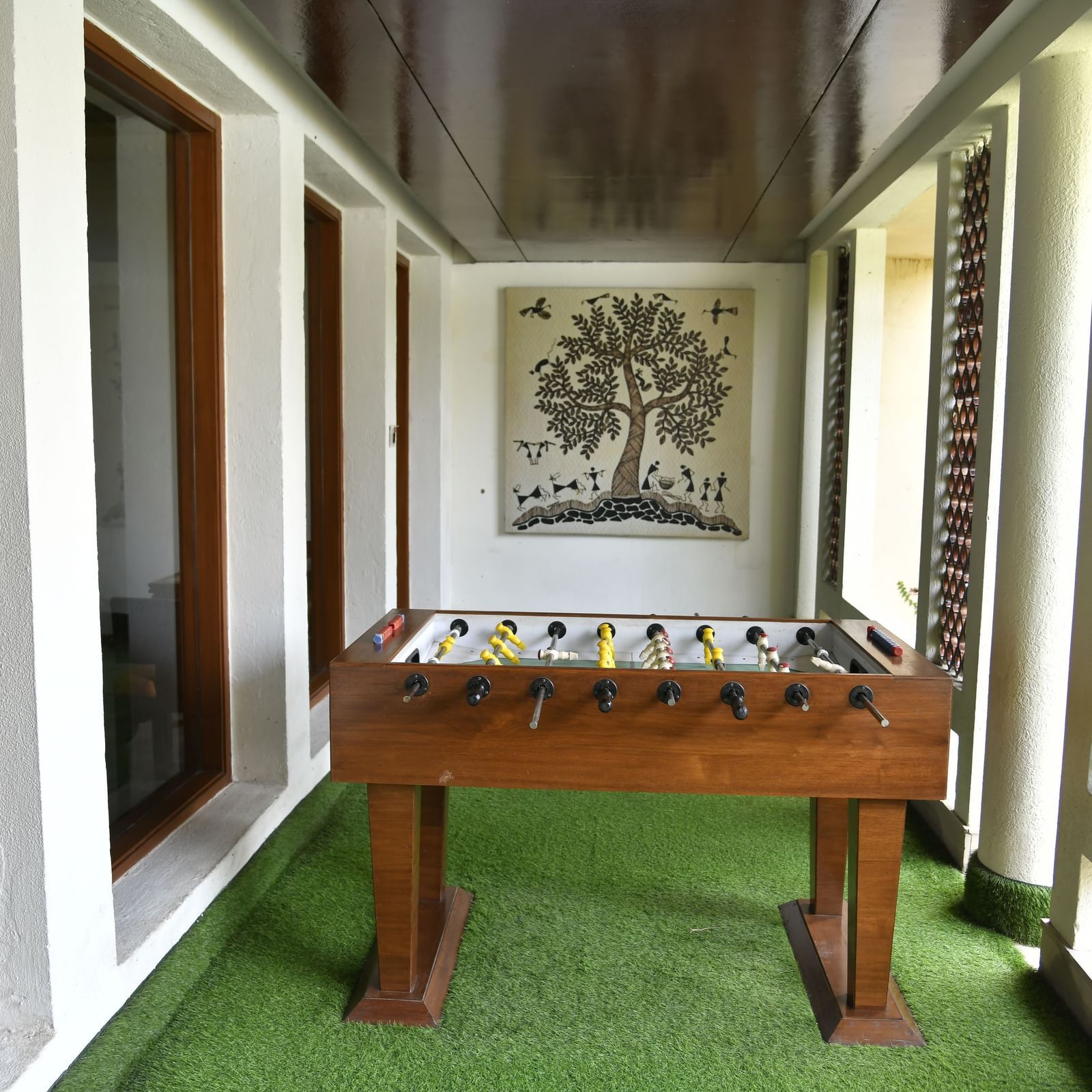 An indoor space features a foosball table and a tree artwork on the wall, with natural light coming through windows