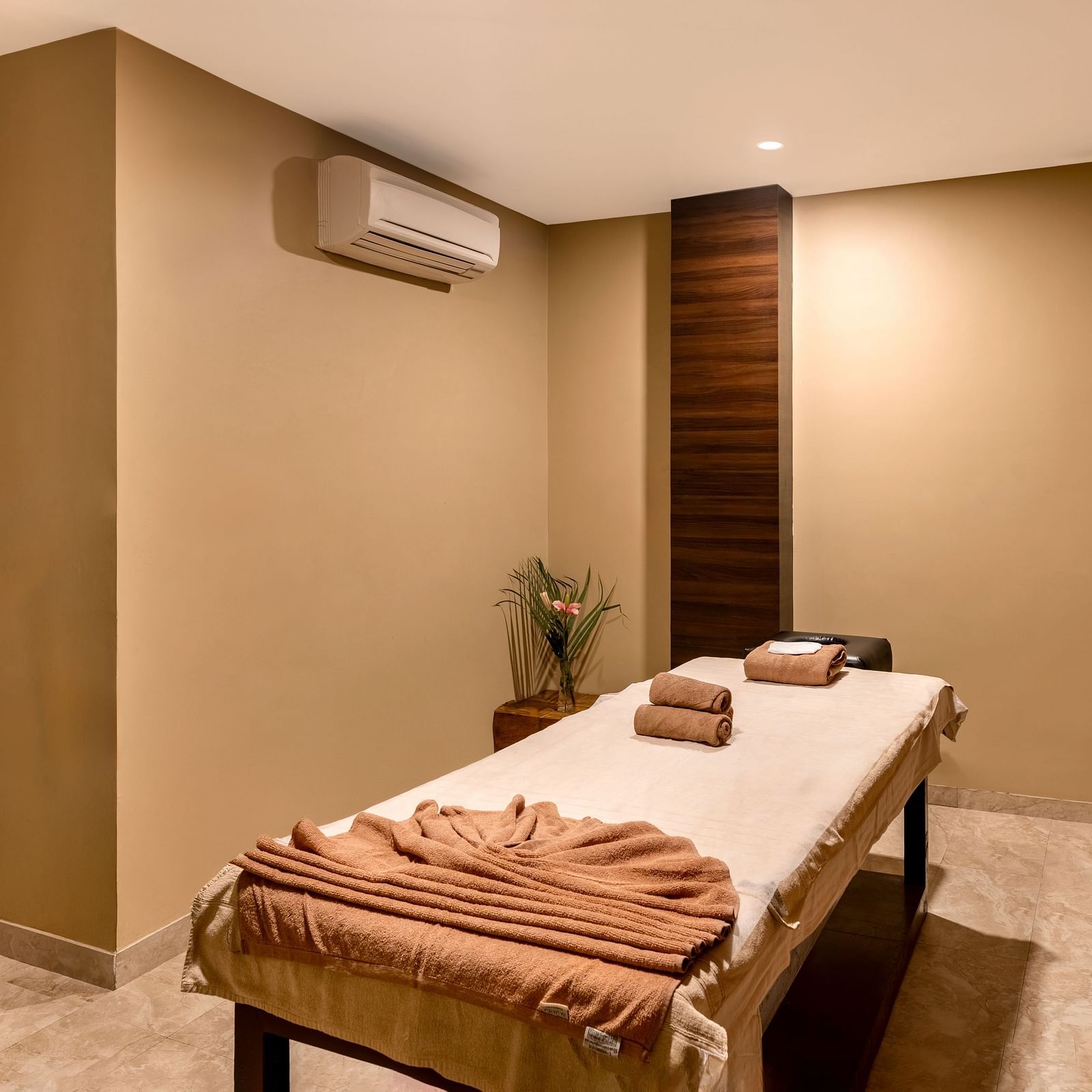 A massage room with a table, towels, and a small flower arrangement - Via Lakhela Resort & Spa, Kumbhalgarh