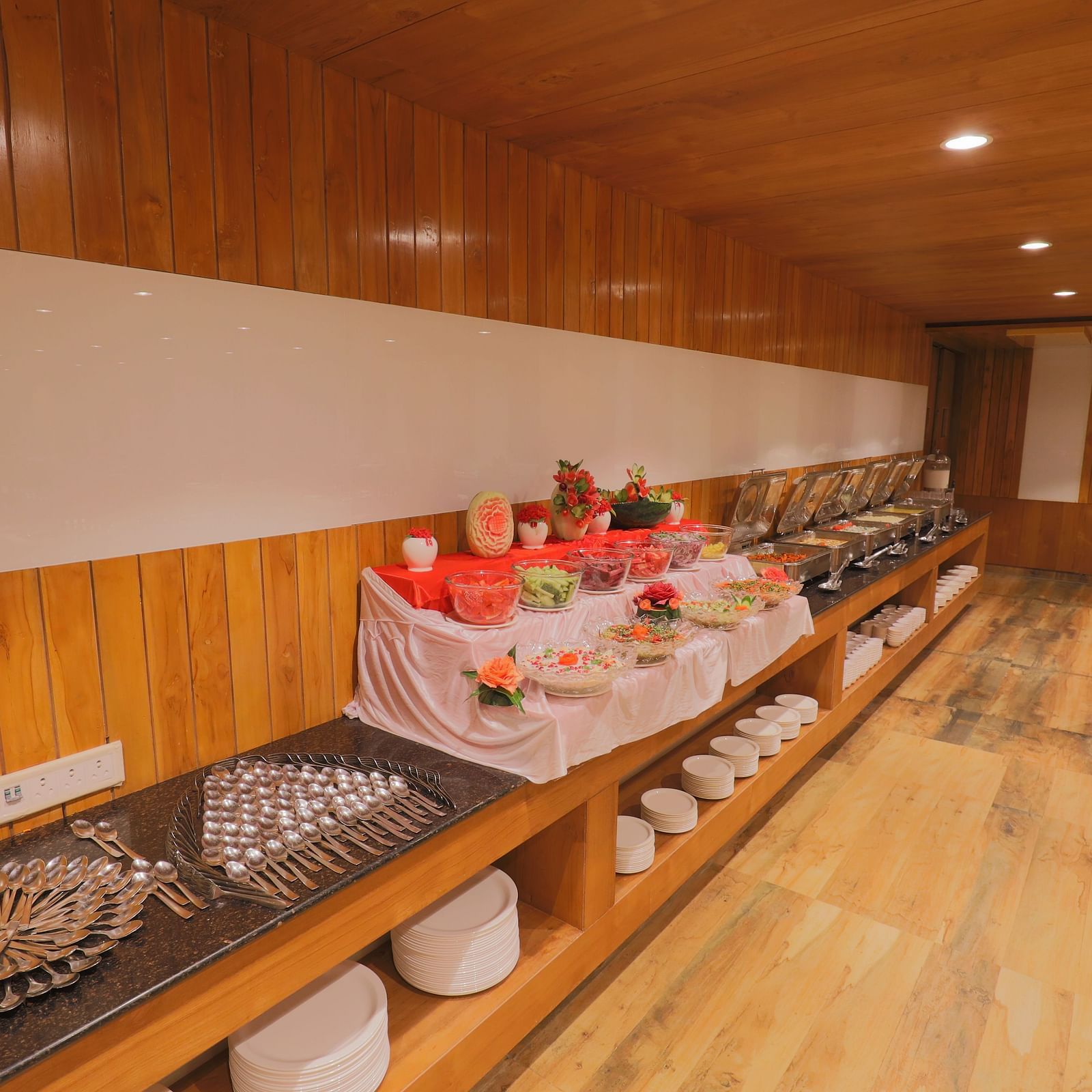 A buffet area with a variety of dishes displayed neatly on a long counter with wooden floor at Vishal Lords Inn Gir Forest