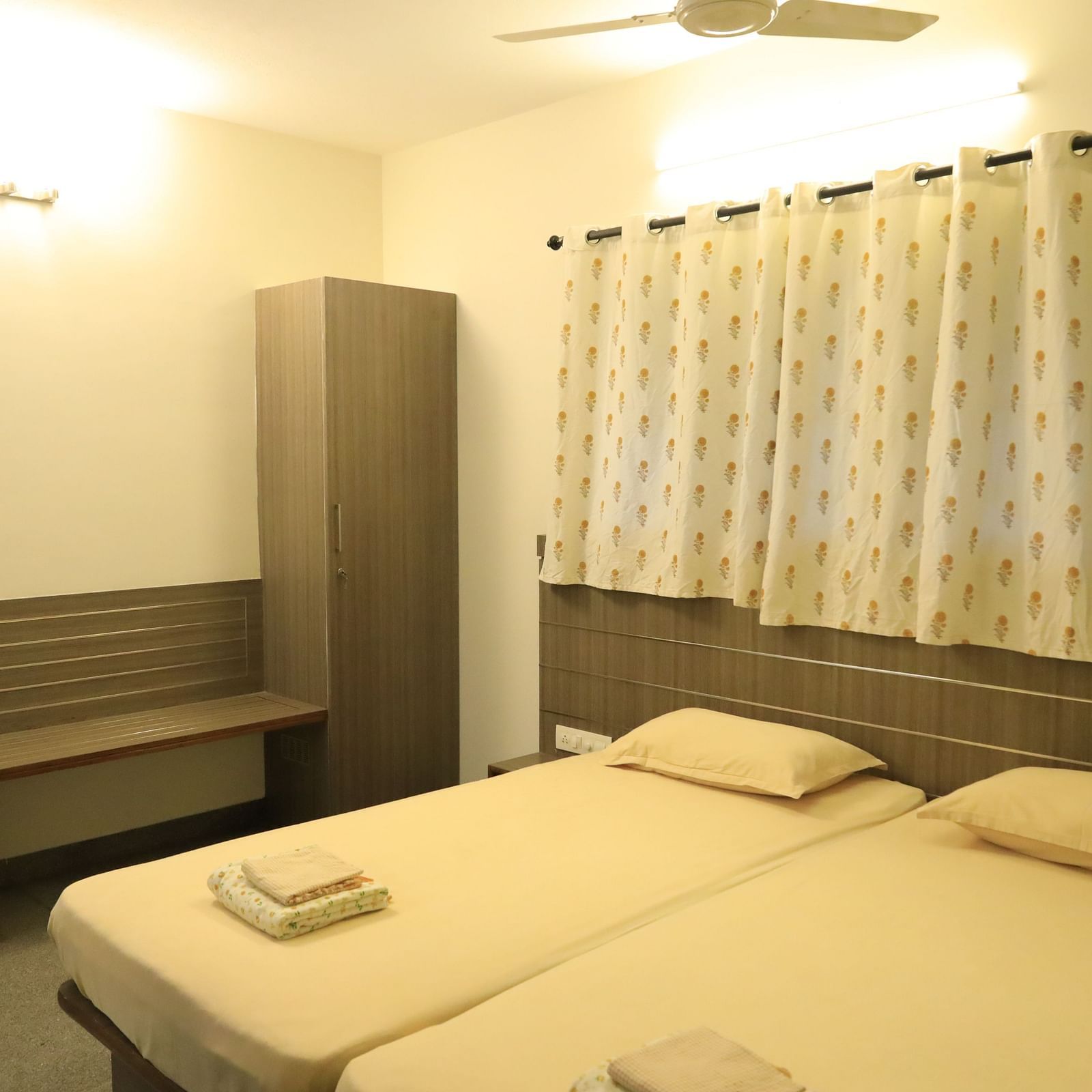 A bedroom at Wyt Hotels Transit Nest, Madurai featuring two single beds, bedside table, and a bench attached to it.