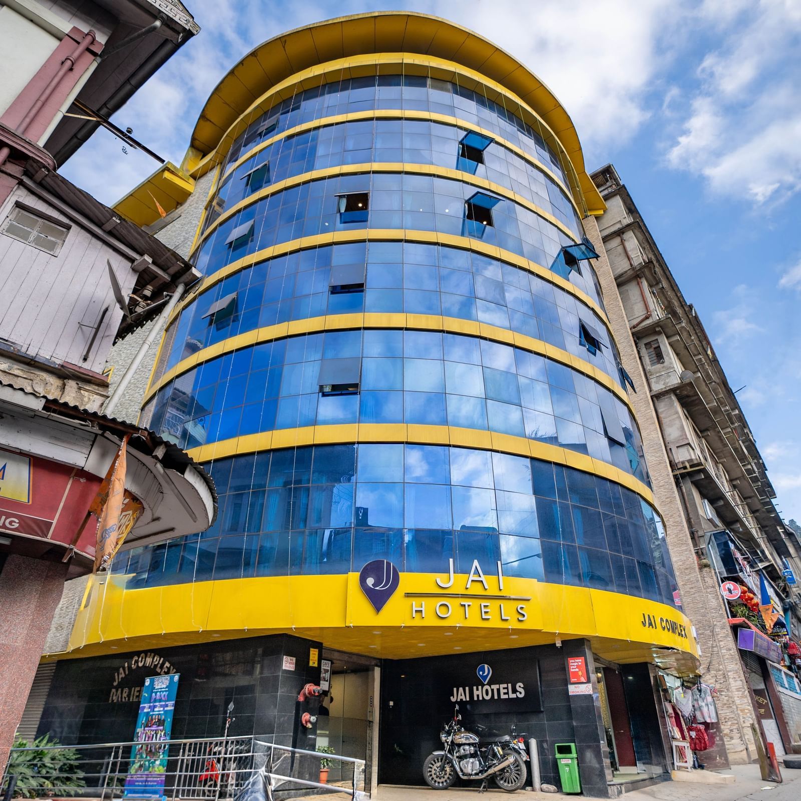 The bright yellow and blue glass exterior of the Yashshree Jai Hotel & Banquet, Darjeeling building.