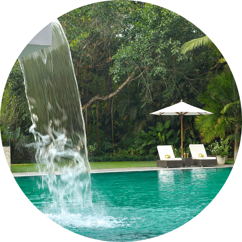 Swimming pool with a waterfall feature surrounded by lush greenery.