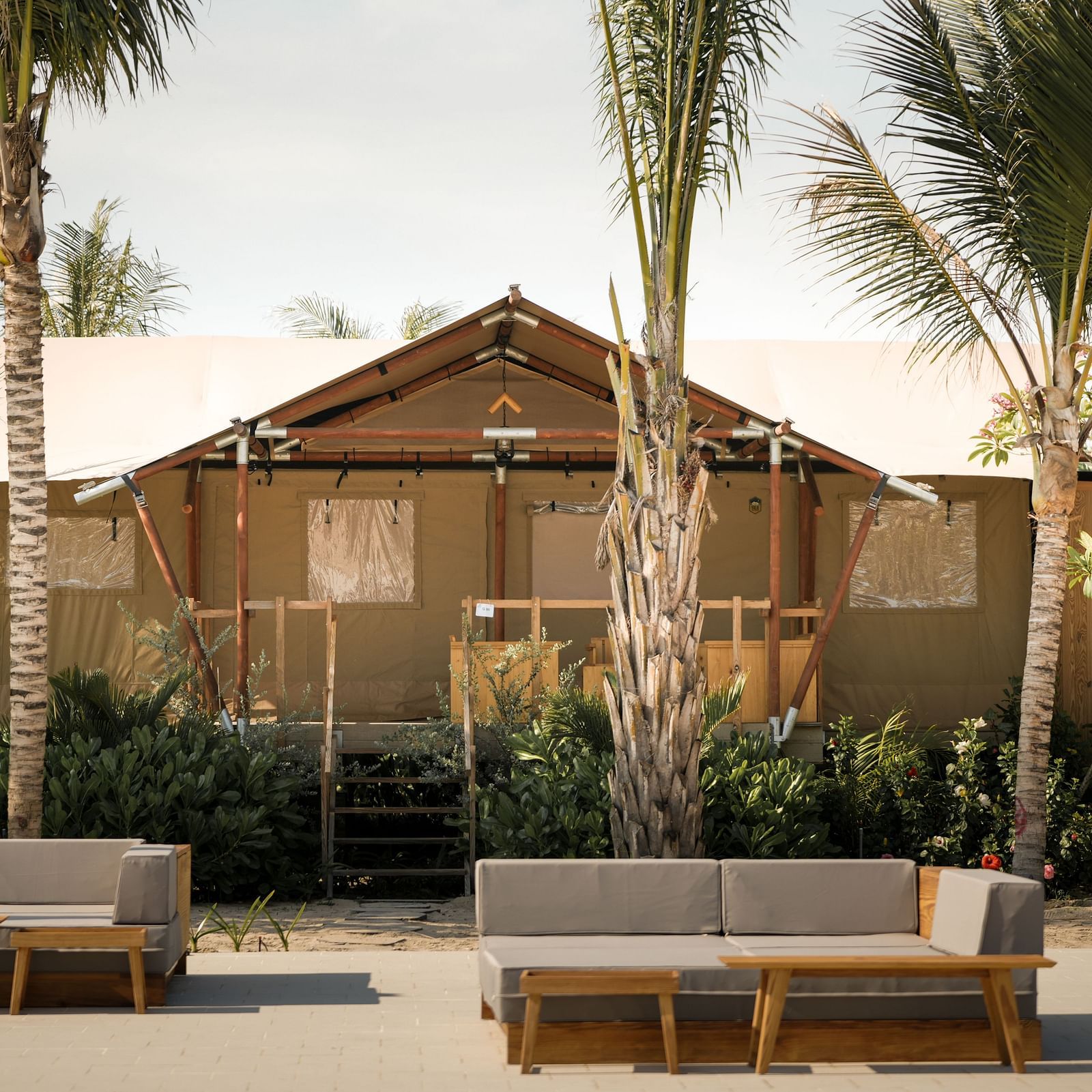 The front view of the Grateful Tent at WoCAL Retreat Ke Ga showcasing a wooden deck with twin daybeds arranged beneath tall palms, evoking a tranquil and welcoming atmosphere.