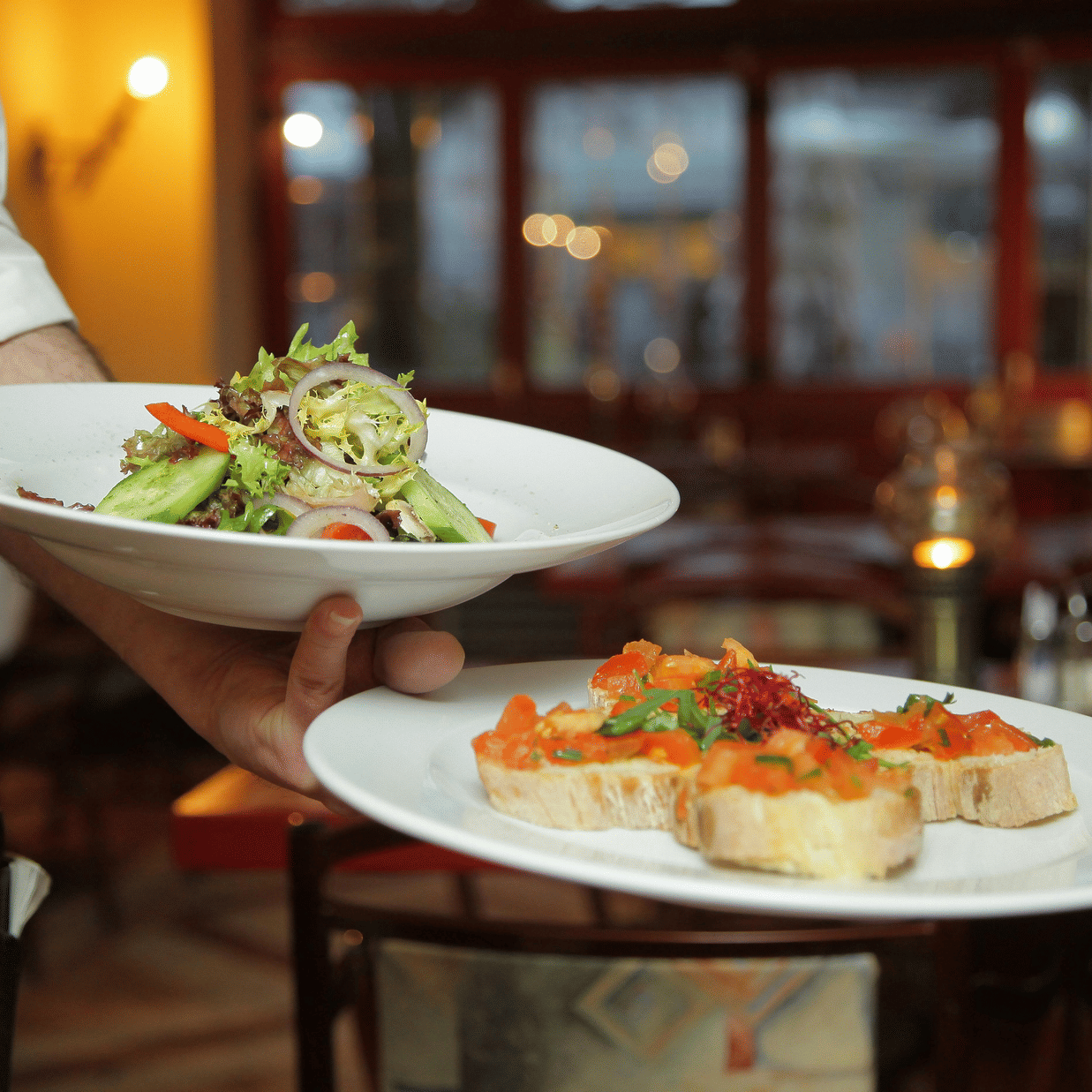 a person in a restaurant holding two plates with delicious cuisines in it that are well plated