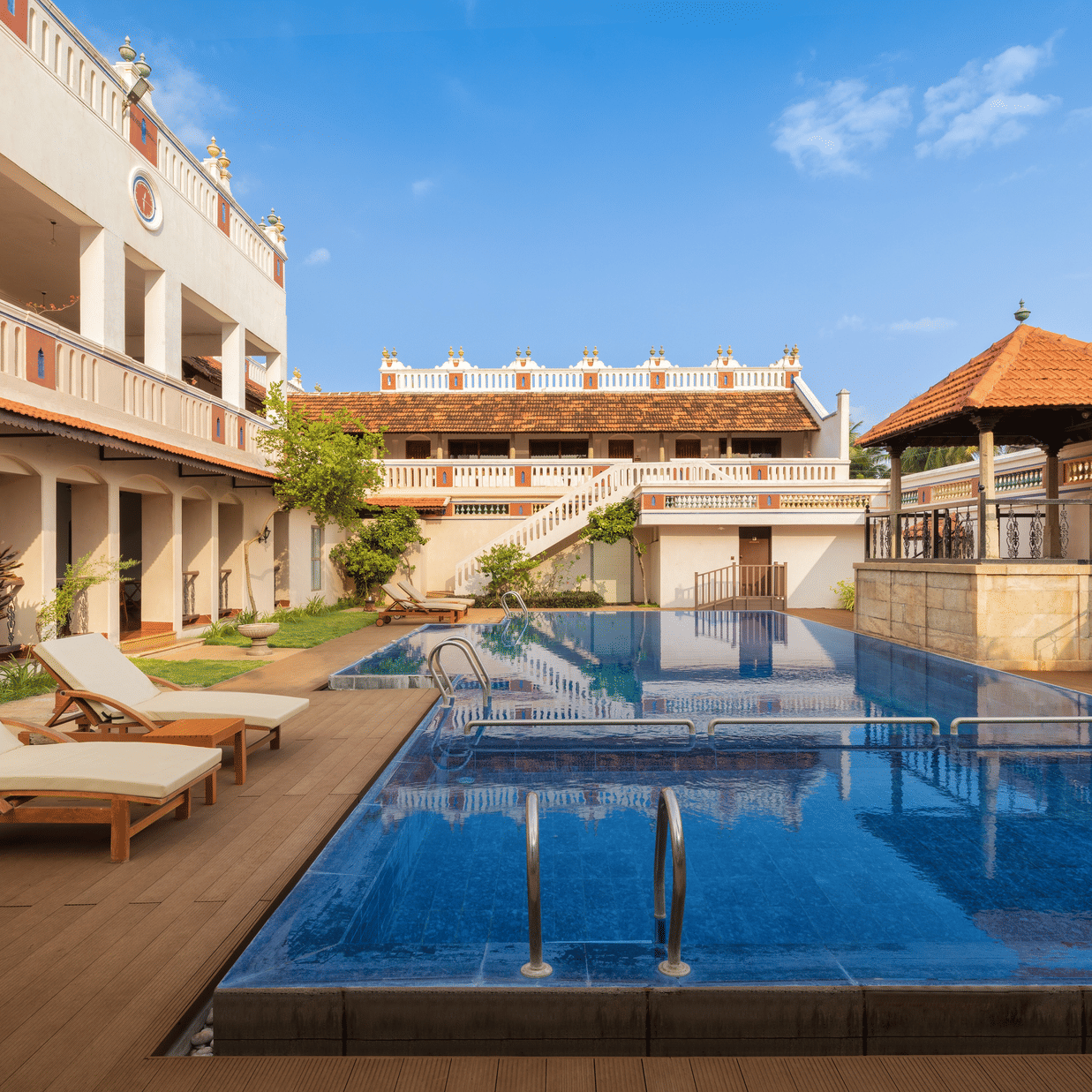 An outdoor swimming pool at Chidambara Vilas Chettinad surrounded by heritage-style architecture with lounge chairs and a shaded pavilion overlooking the courtyard.