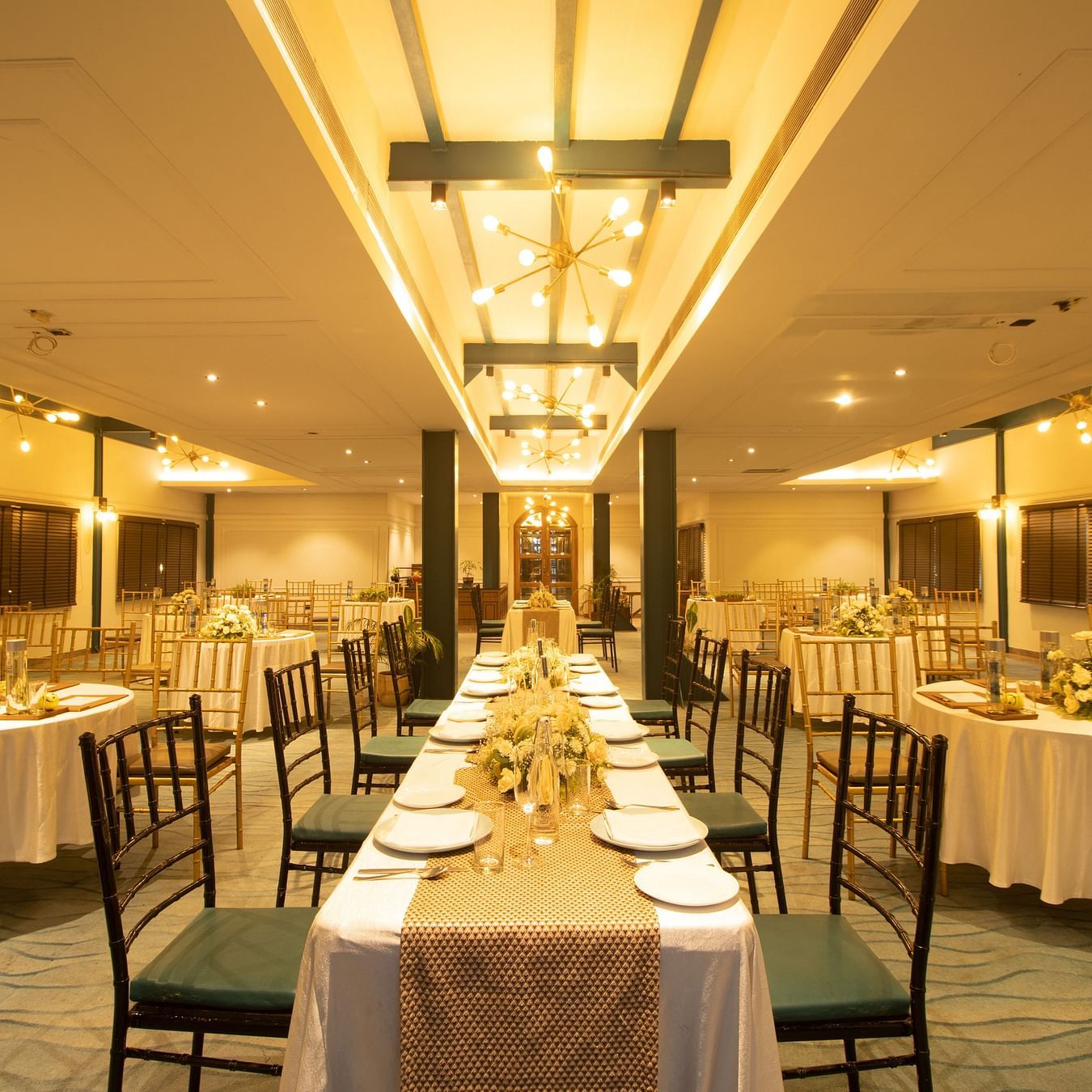 Banquet room with round and rectangular tables, sophisticated table settings, and striking ceiling lights.