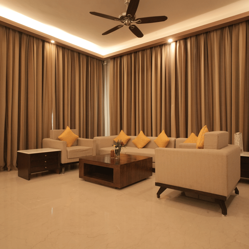 A living room with comfortable sofas, a center table, floor-to-ceiling curtains, and warm lighting in the Presidential Suite at Clarks Amer, Jaipur.