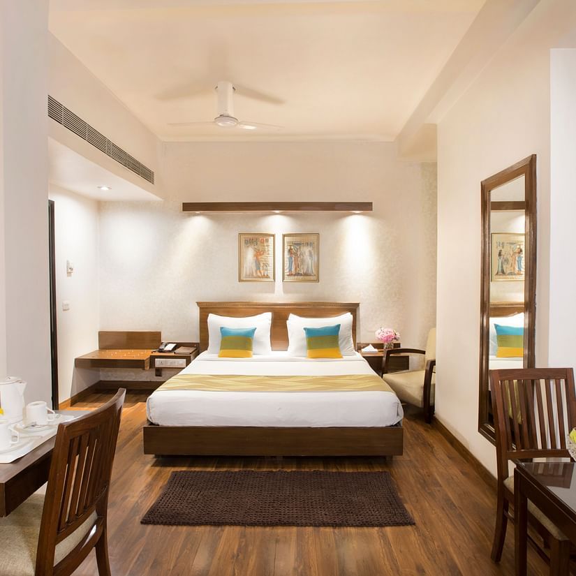 Spacious hotel room at Rockland Hotel, Panchsheel Enclave, New Delhi, with plush bed, wooden flooring, elegant decor, and cosy seating area.