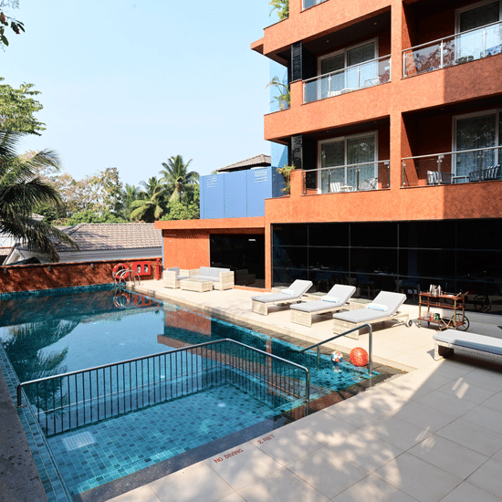 The outdoor swimming pool area with lounging chairs placed besides it at Golden Tulip Vagator, Goa