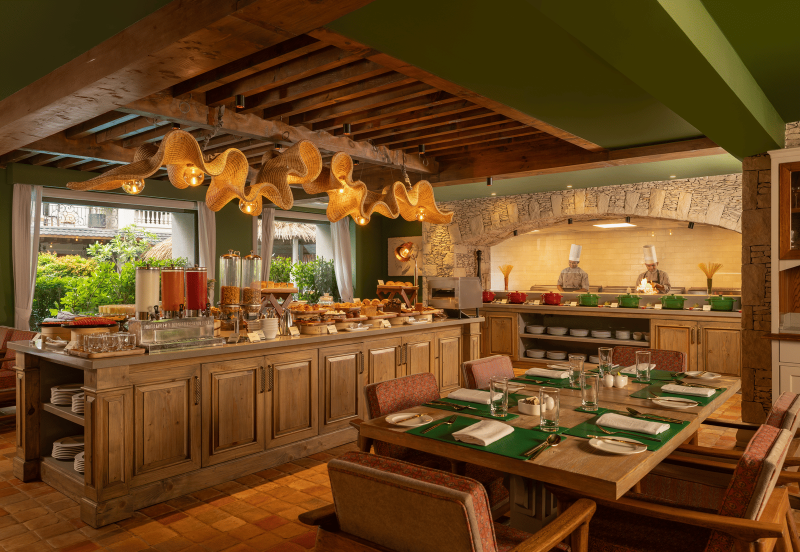 A wide-angle shot of Mila Restaurant at The Evren, Vagator, featuring a buffet counter in the middle of the dining area surrounded with well-arranged tables with cutlery and napkins.
